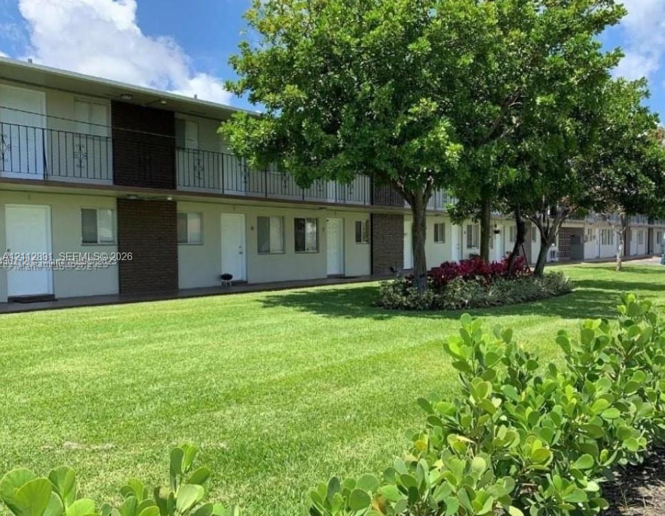 Two-story exterior featuring a metal balcony, manicured lawn, mature trees, and curated landscaping