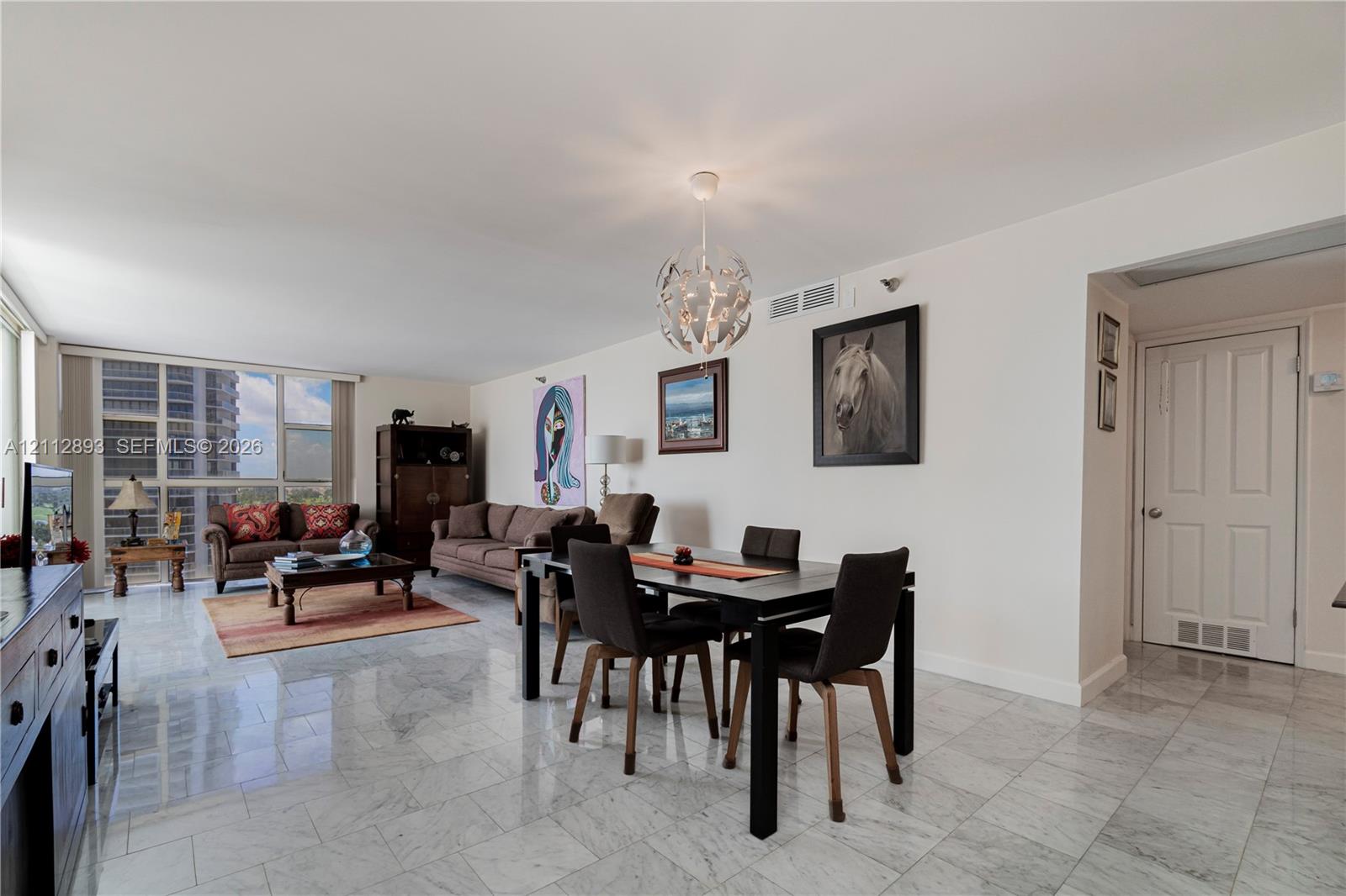 Open-concept interior featuring light-toned stone flooring, floor-to-ceiling windows, and a spherical multi-light pendant fixture