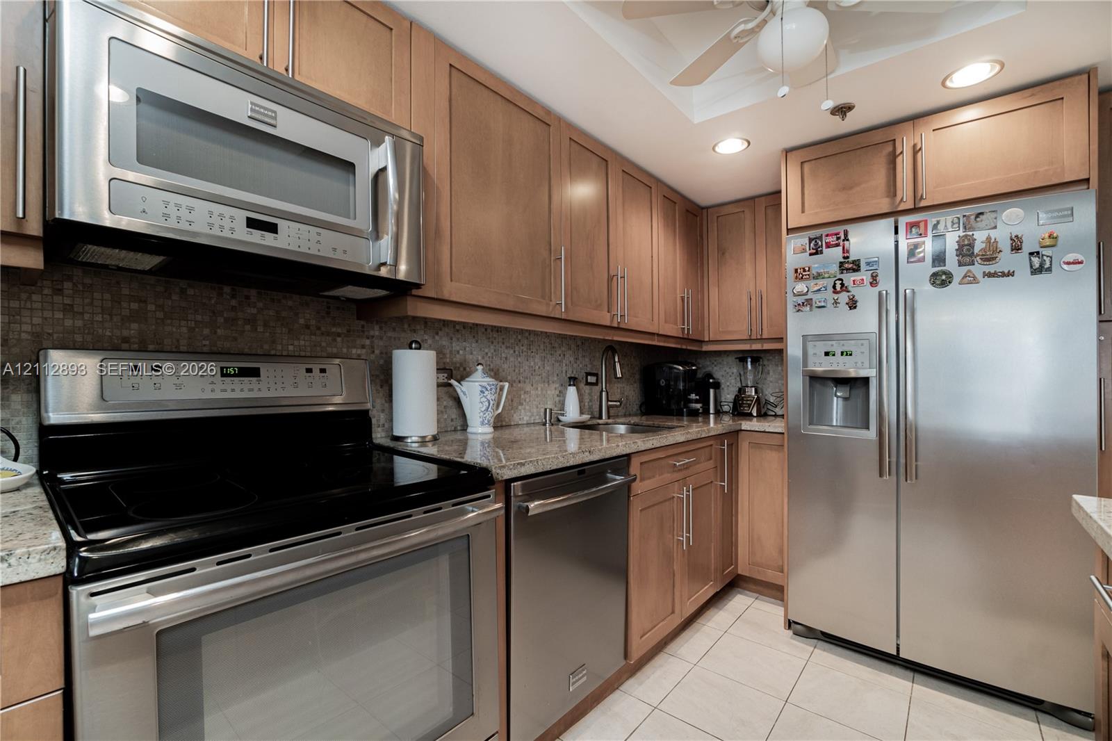 Kitchen featuring wood cabinetry, stone countertops, a mosaic tile backsplash, stainless steel appliances, and tile flooring