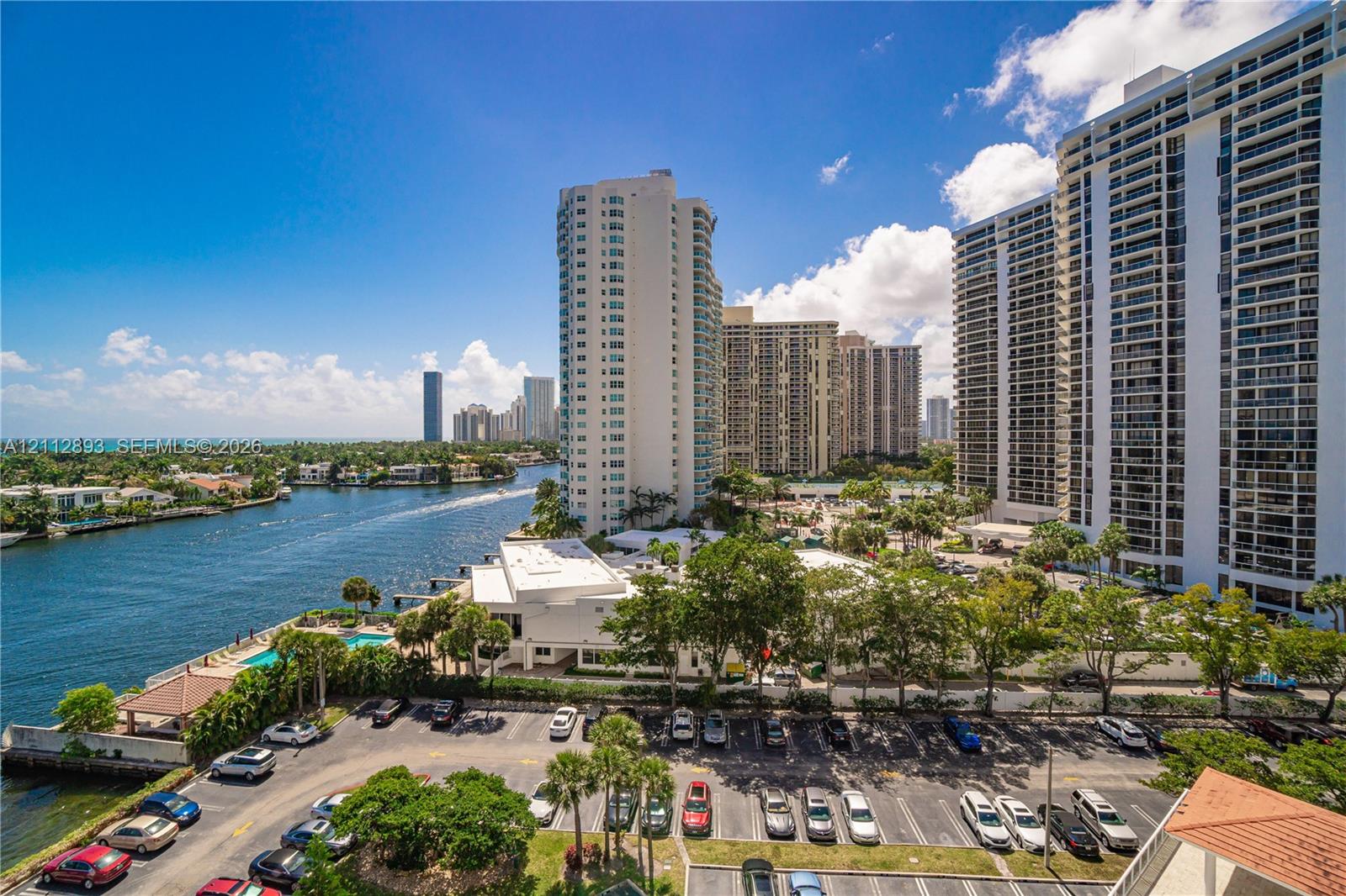 High-rise vantage point featuring a waterway, mature palm trees, paved parking area, and coastal landscape