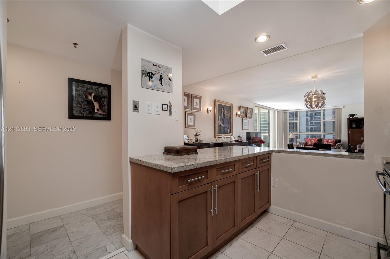 Kitchen area featuring wooden cabinetry with stainless steel bar pulls, stone-composite countertops, recessed lighting, and tile flooring