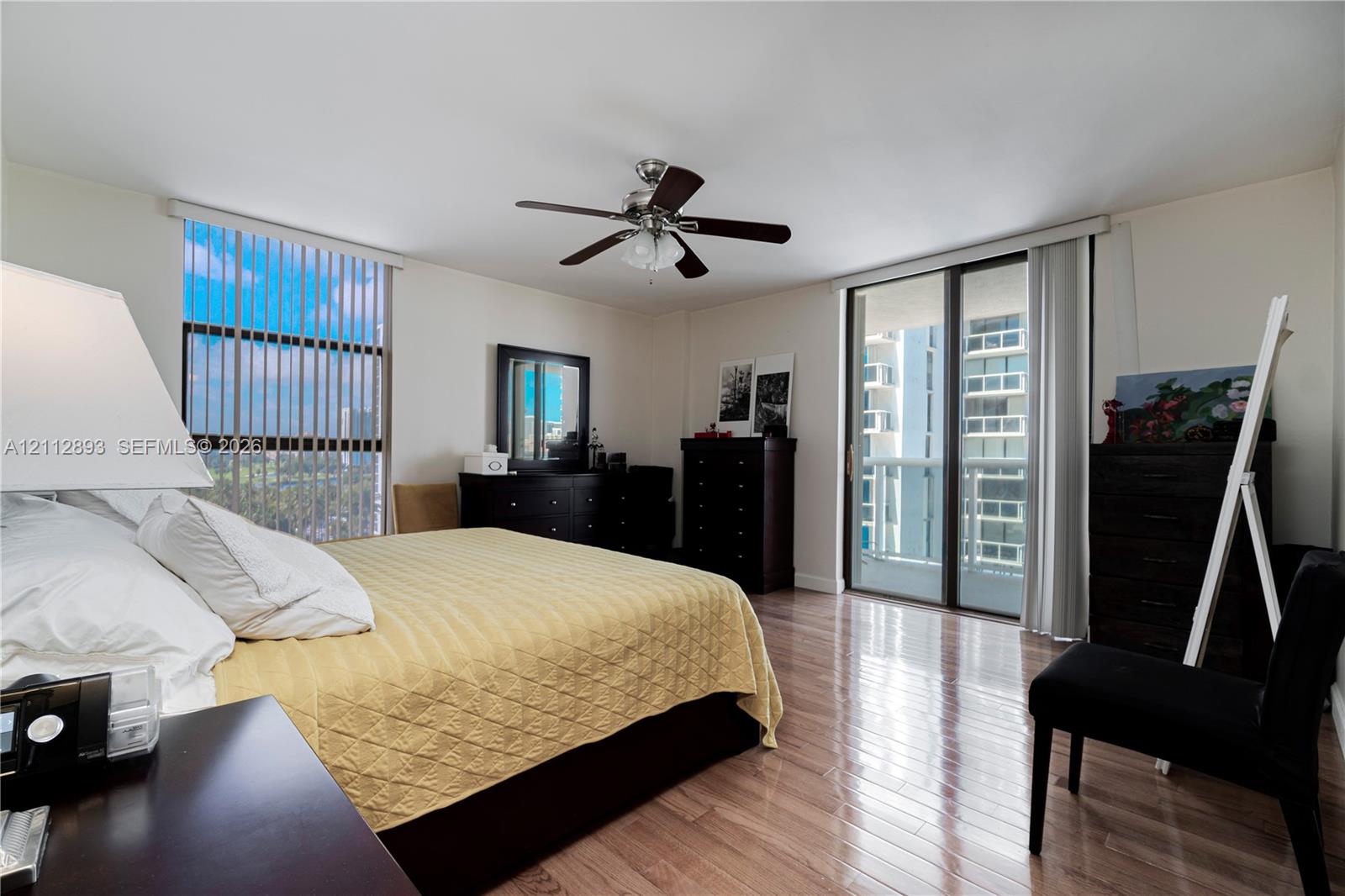 Wood-finish flooring, ceiling fan with integrated lighting, large vertical window with blinds, and sliding glass door with access to a balcony