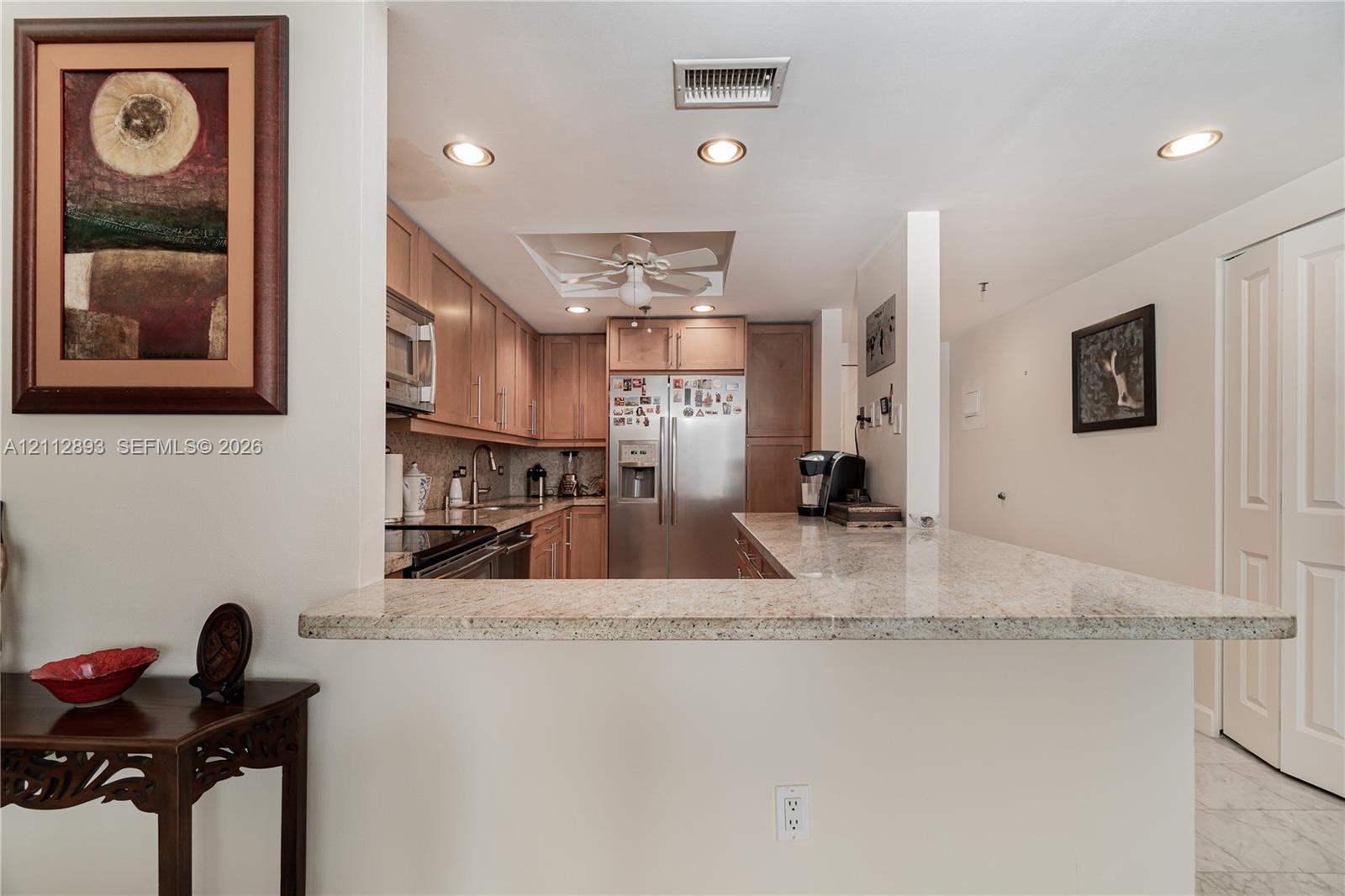 Kitchen featuring stone-finish countertops, stainless steel appliances, light wood cabinetry, recessed lighting, and a breakfast bar