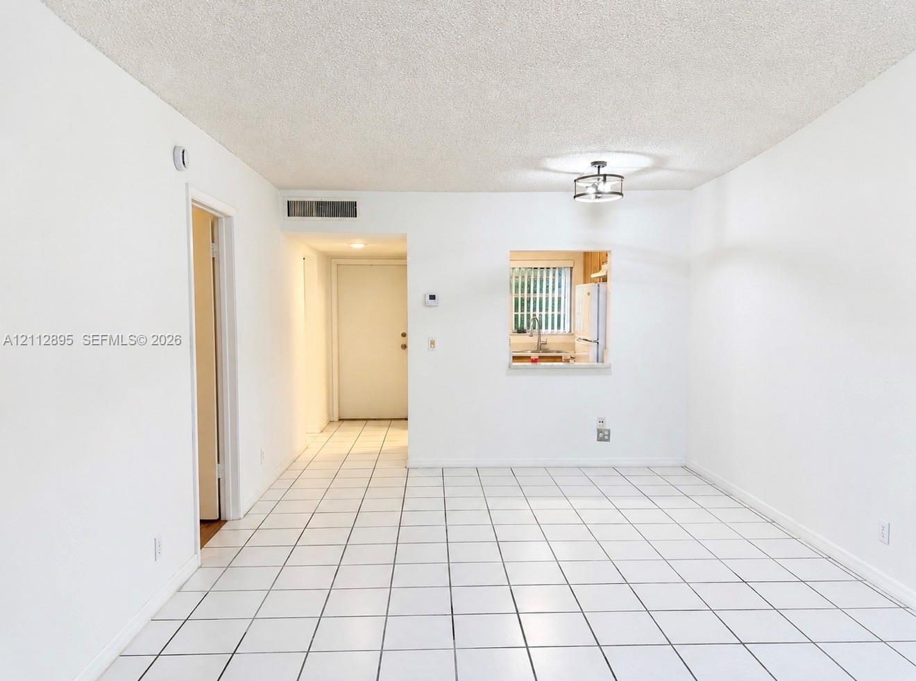Interior space featuring large-format square tile flooring, a pass-through window to the kitchen, and a circular drum-style ceiling light fixture