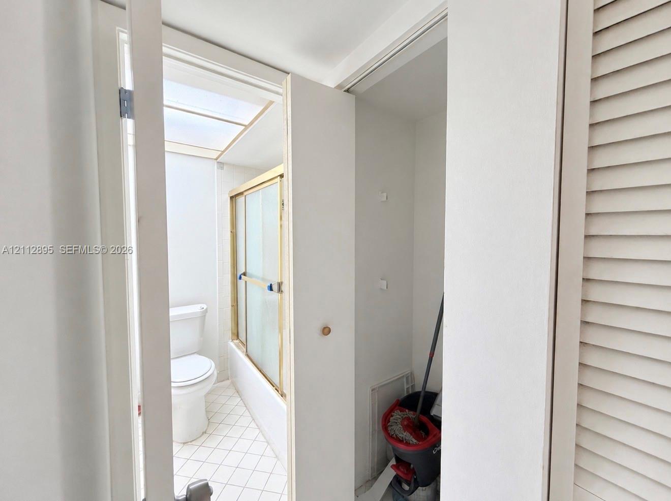 Bathroom featuring a skylight, a shower-tub combination with a metal-framed enclosure, a standard white toilet, and tile flooring