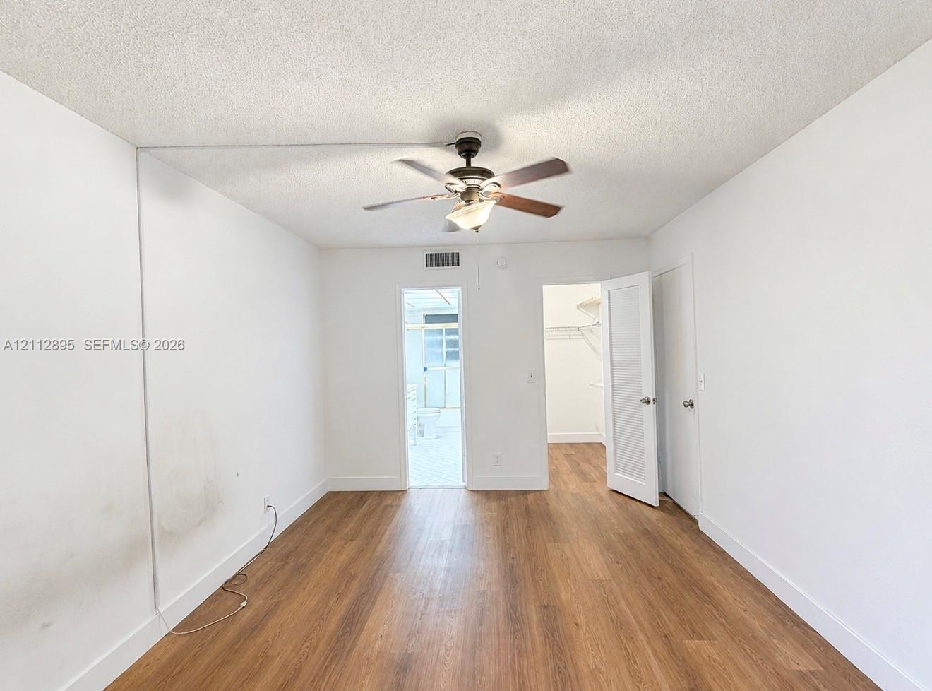 Room featuring wood-finish flooring, a ceiling fan with integrated lighting, and a walk-in closet with built-in shelving