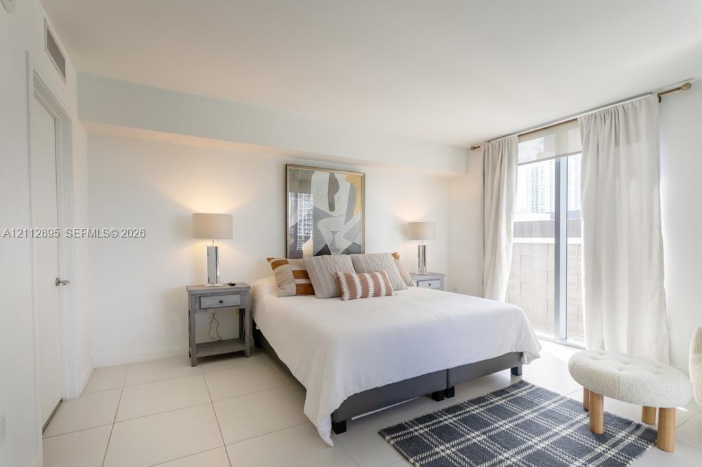 Neutral-toned ceramic tile flooring, floor-to-ceiling windows with curtain rod hardware, and recessed ceiling lighting