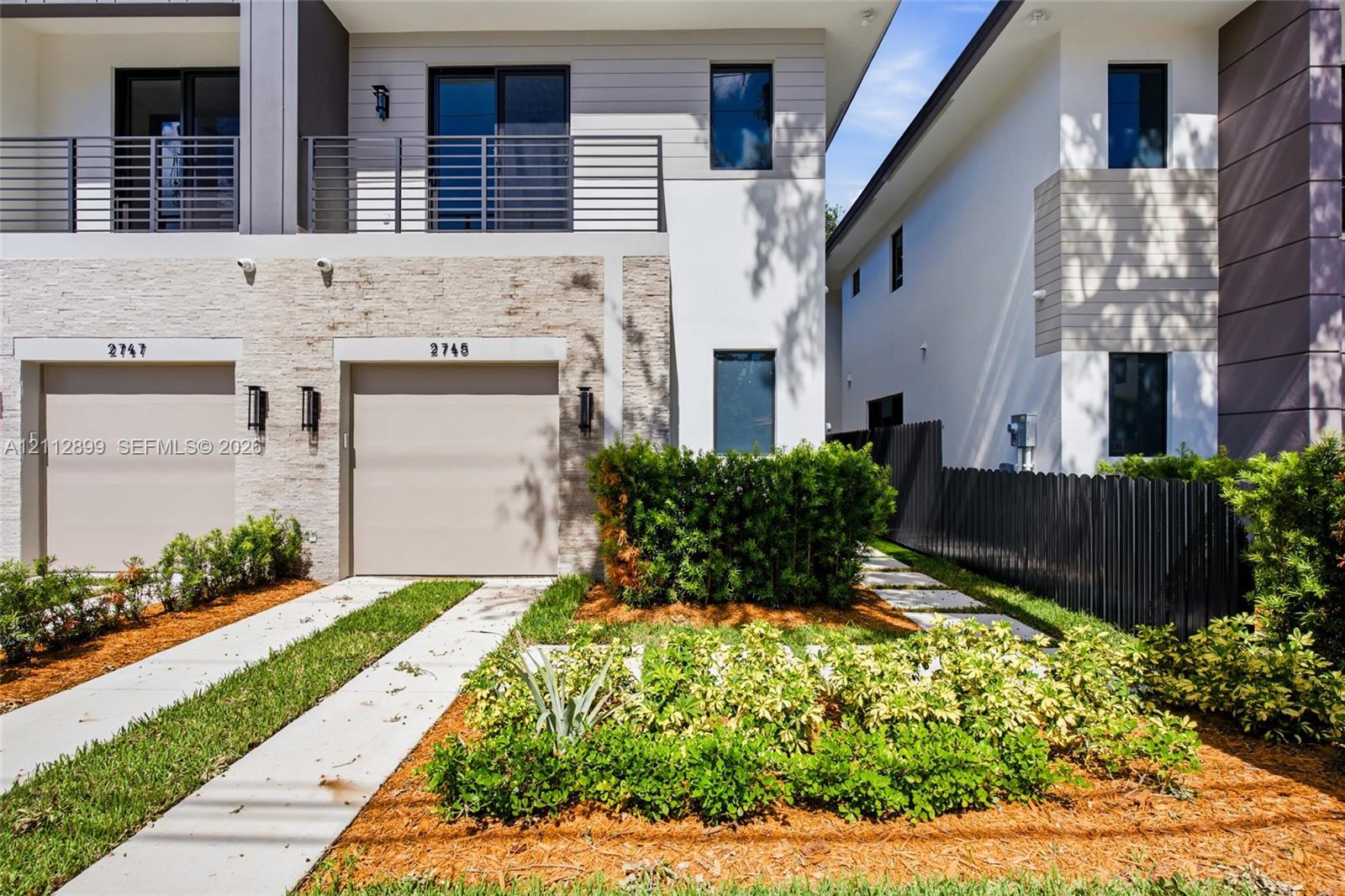 Modern exterior featuring stone veneer siding, a second-story balcony with metal railings, horizontal lap siding, and a concrete driveway with a central grass strip Modern exterior featuring stone veneer siding, a second-story balcony with metal railings, horizontal lap siding, and a concrete driveway with a central grass strip