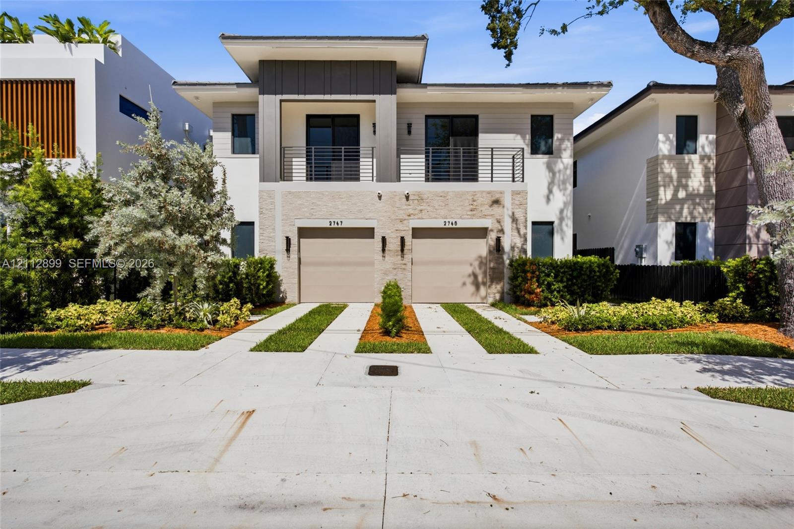 Contemporary two-story exterior featuring a horizontal-slat facade, stone veneer detailing, metal balcony railing, and two integrated garage doors
