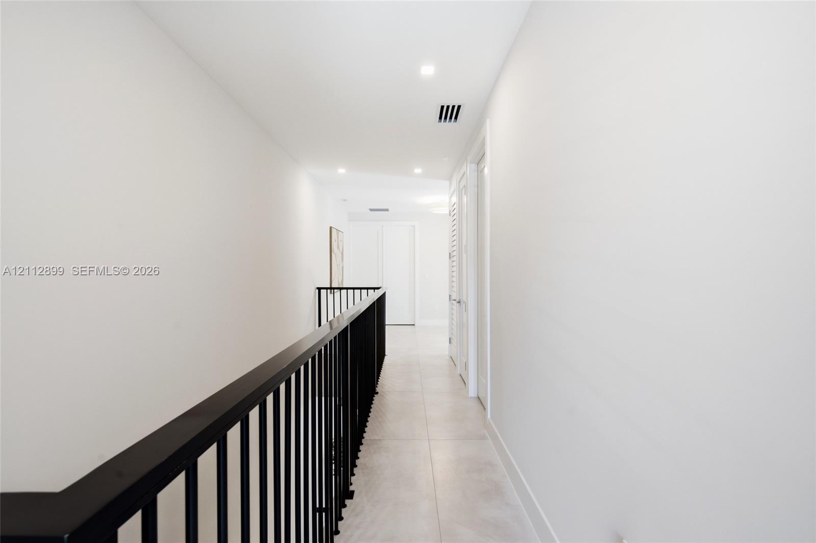 Hallway featuring large-format tile flooring, matte black metal railing, and recessed ceiling lighting