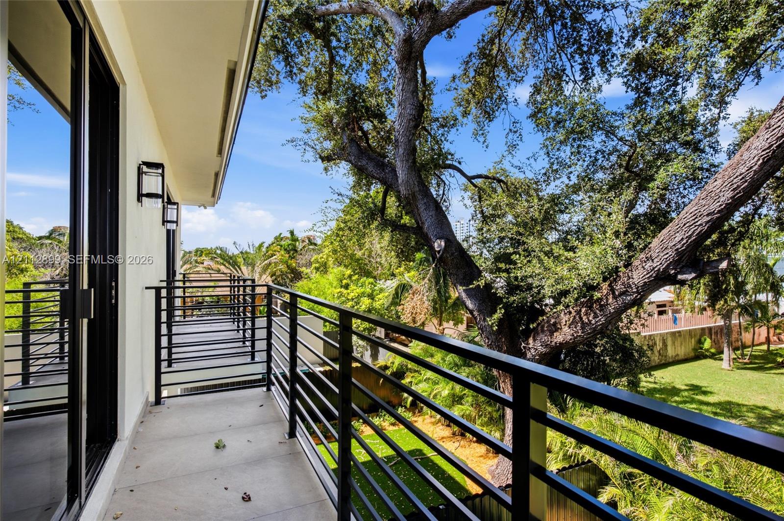 Covered balcony featuring matte black metal railings, concrete flooring, and wall-mounted exterior lighting