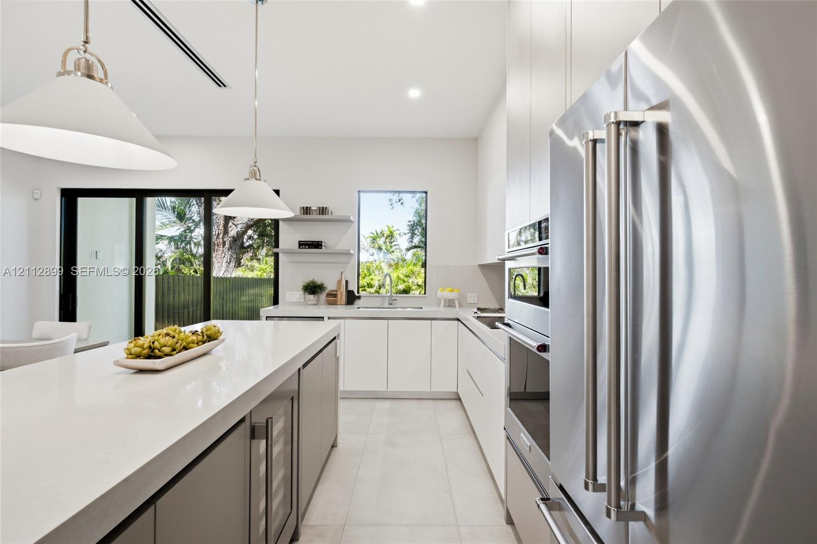 Kitchen featuring quartz countertops, flat-panel cabinetry, stainless steel built-in appliances, a wine refrigerator, and pendant lighting