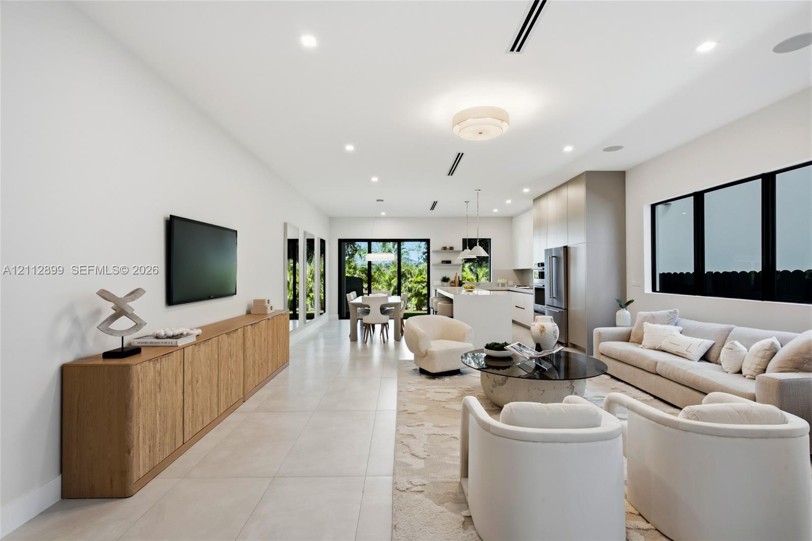 Open-concept living space featuring large-format tile flooring, recessed lighting, expansive glass sliding doors, built-in cabinetry, and a kitchen island with stone countertops Open-concept living space featuring large-format tile flooring, recessed lighting, expansive glass sliding doors, built-in cabinetry, and a kitchen island with stone countertops