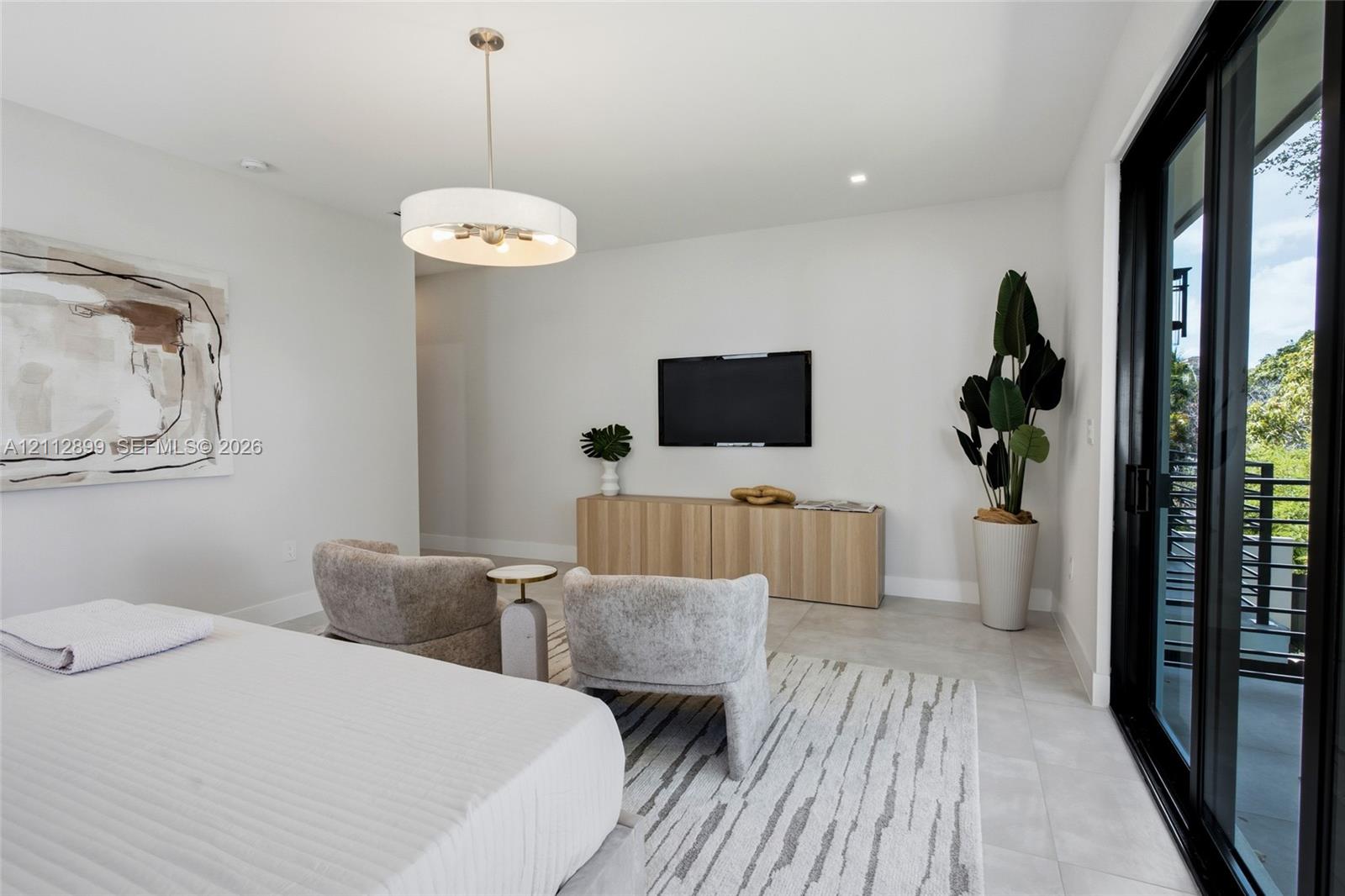 Neutral-toned interior featuring large-format tile flooring, a contemporary drum pendant light fixture, and black-framed sliding glass doors opening to an exterior balcony