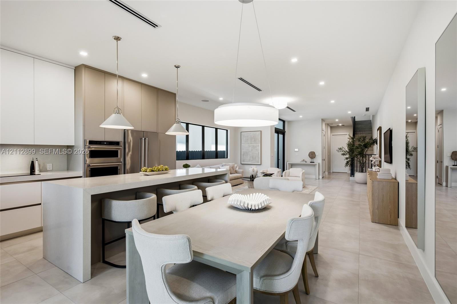 Open-concept kitchen featuring flat-panel cabinetry, a waterfall-edge stone island, built-in double ovens, and large-format tile flooring