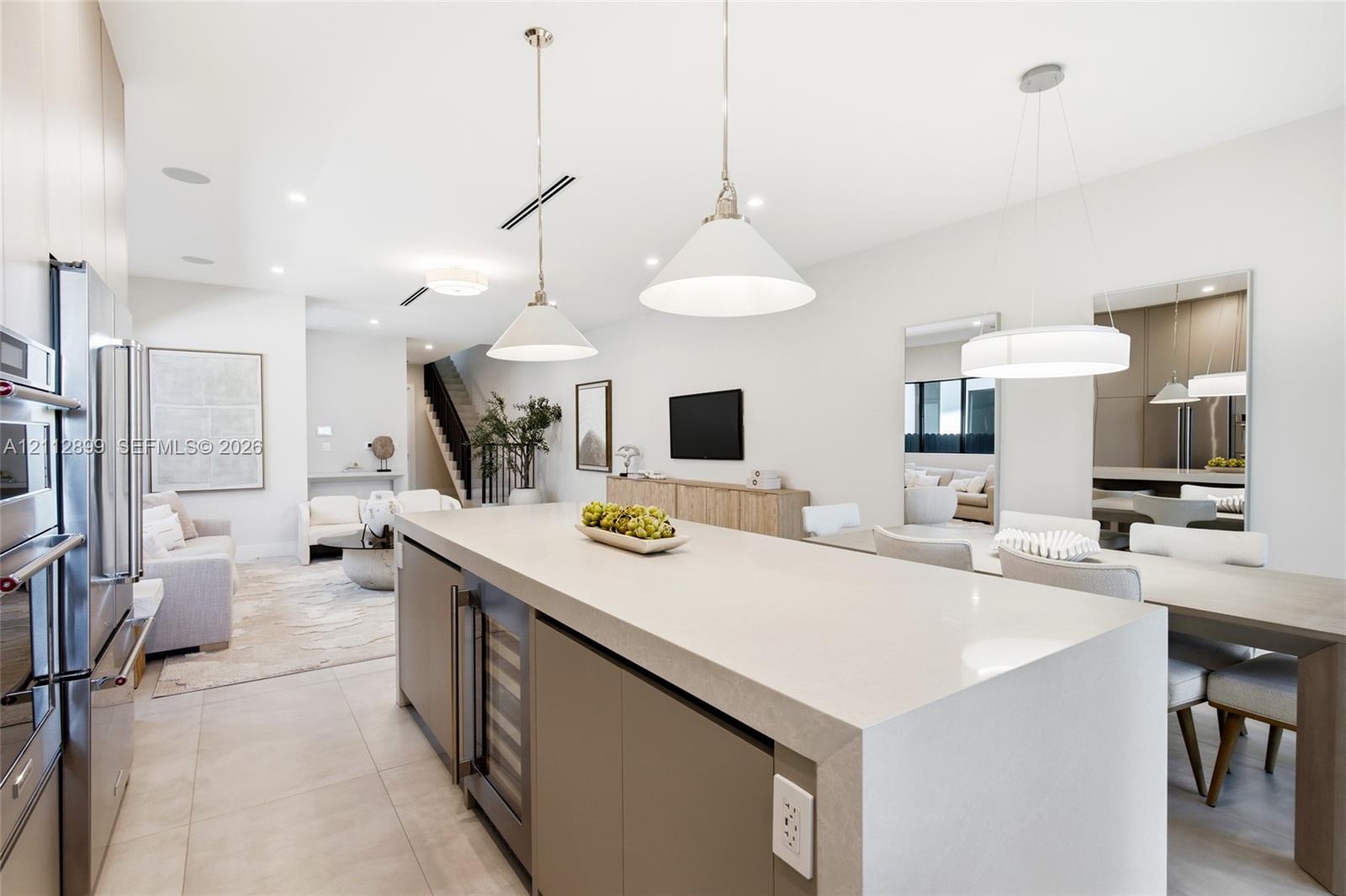 Large kitchen island with quartz waterfall countertop, integrated wine refrigerator, recessed lighting, matte-finish cabinetry, and oversized pendant fixtures