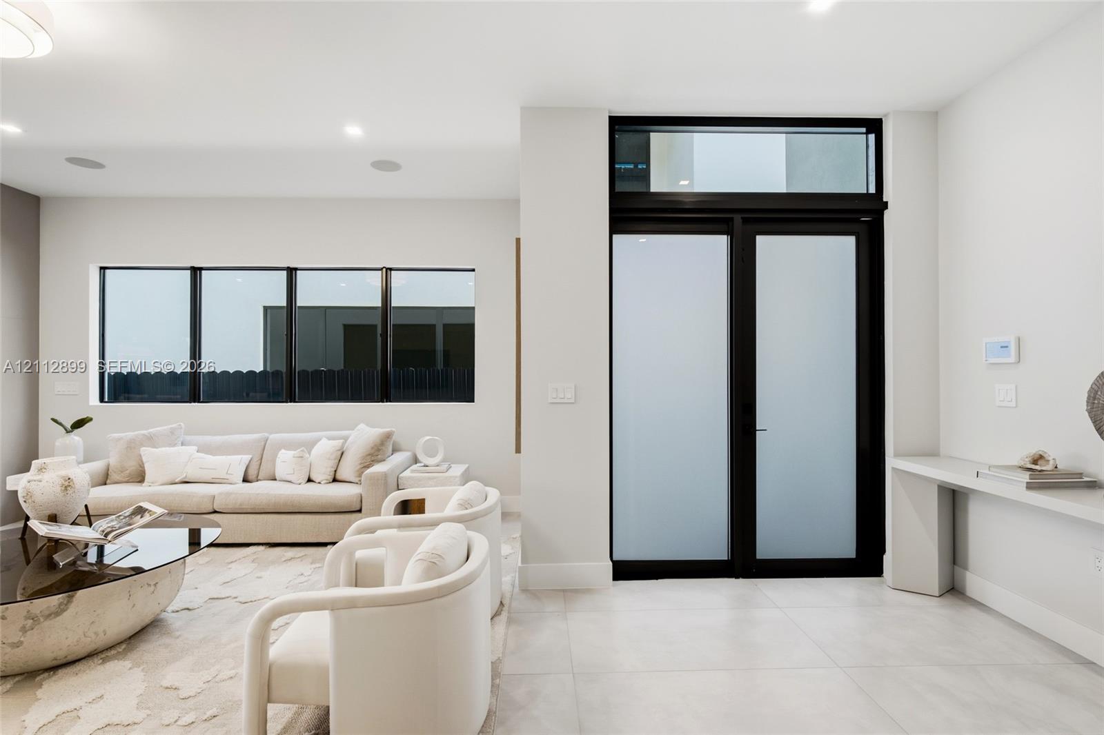 Double entry doors with frosted glass panels and an overhead transom window, large-format tile flooring, recessed lighting, and a built-in wall-mounted console Double entry doors with frosted glass panels and an overhead transom window, large-format tile flooring, recessed lighting, and a built-in wall-mounted console