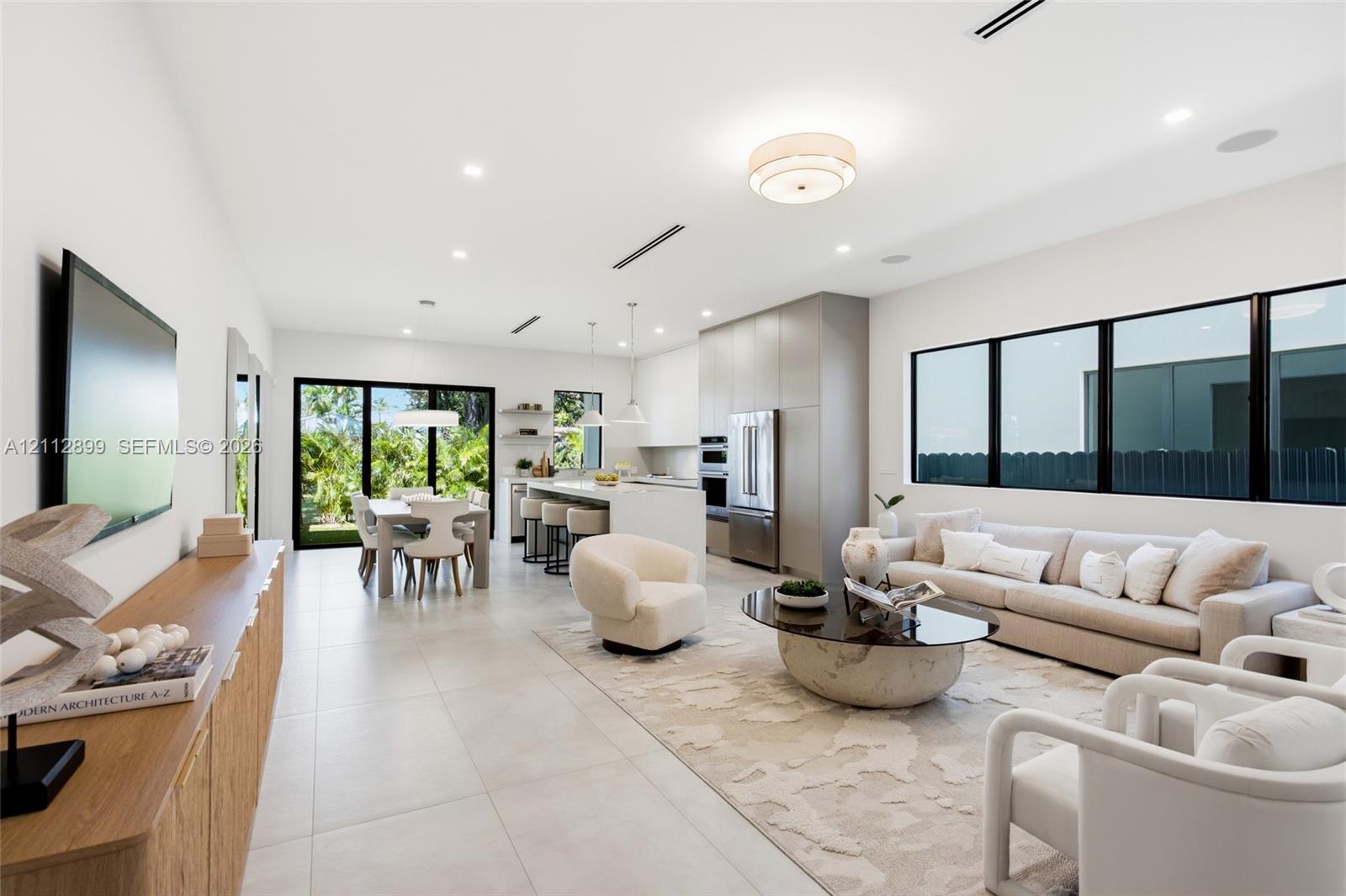 Open-concept interior featuring large-format tile flooring, recessed ceiling lighting, built-in kitchen cabinetry, stainless steel appliances, and black-framed windows Open-concept interior featuring large-format tile flooring, recessed ceiling lighting, built-in kitchen cabinetry, stainless steel appliances, and black-framed windows