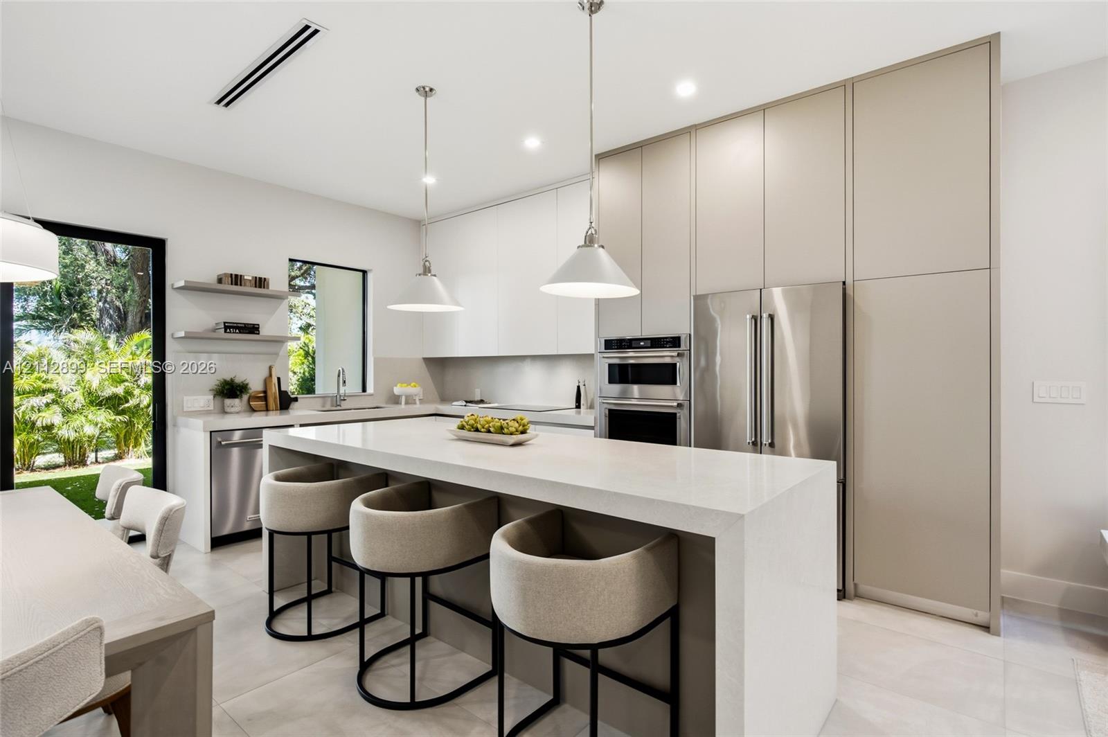 Contemporary kitchen featuring floor-to-ceiling flat-panel cabinetry, a waterfall-edge stone island, built-in stainless steel appliances, and dual pendant lighting Contemporary kitchen featuring floor-to-ceiling flat-panel cabinetry, a waterfall-edge stone island, built-in stainless steel appliances, and dual pendant lighting
