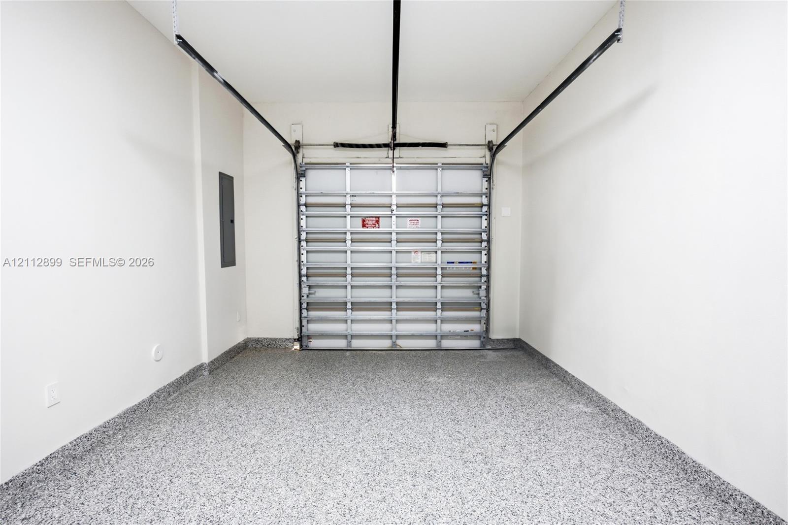 Enclosed garage space featuring a metal overhead door, seamless speckled epoxy flooring, and crisp white wall finishes