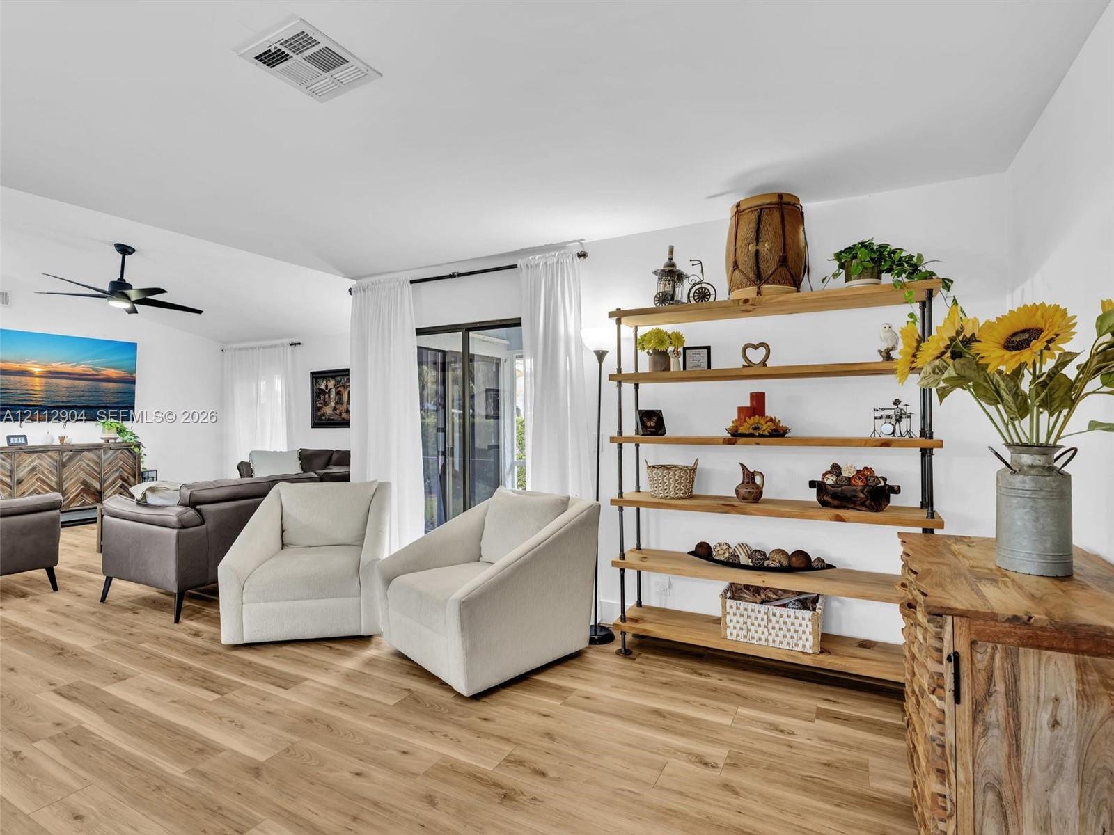 Open-concept interior featuring wood-finish flooring, vaulted ceilings, a ceiling fan, and sliding glass doors