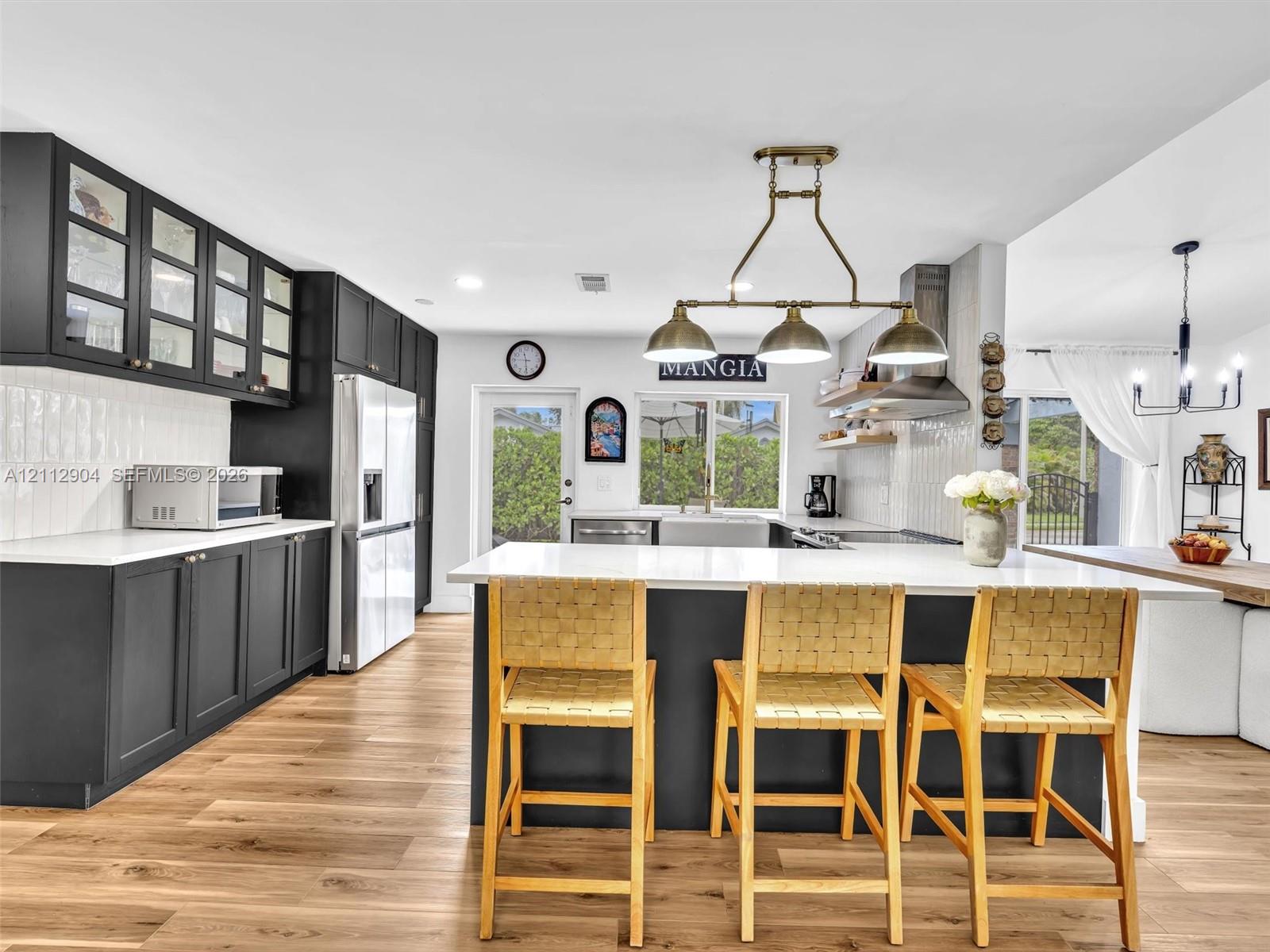 Kitchen featuring flat-panel cabinetry with glass-front uppers, a central island with a solid-surface countertop, wood-finish flooring, and multi-bulb pendant lighting