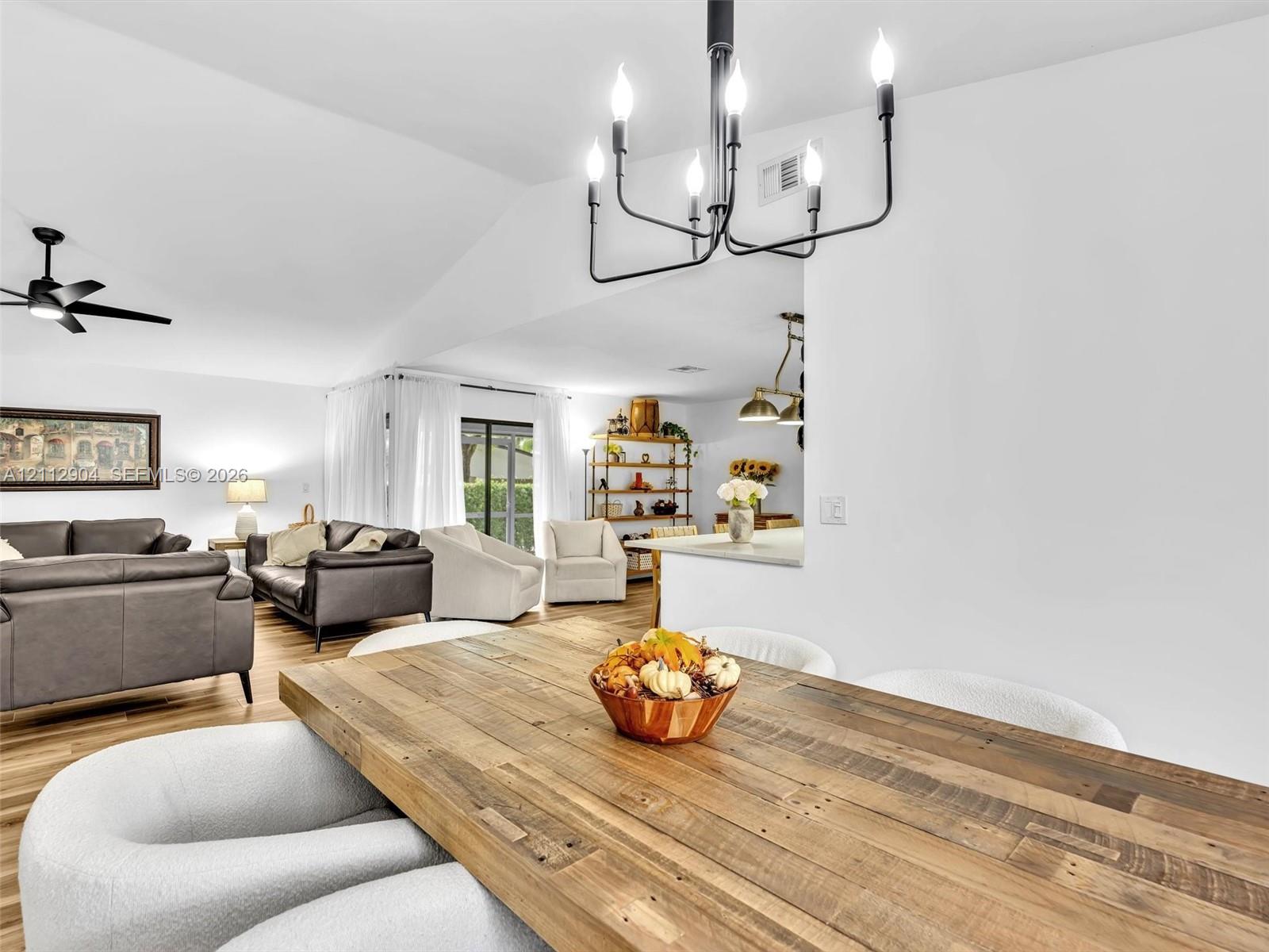 Vaulted ceilings, matte black metal chandelier, ceiling fan, and wood-finish flooring