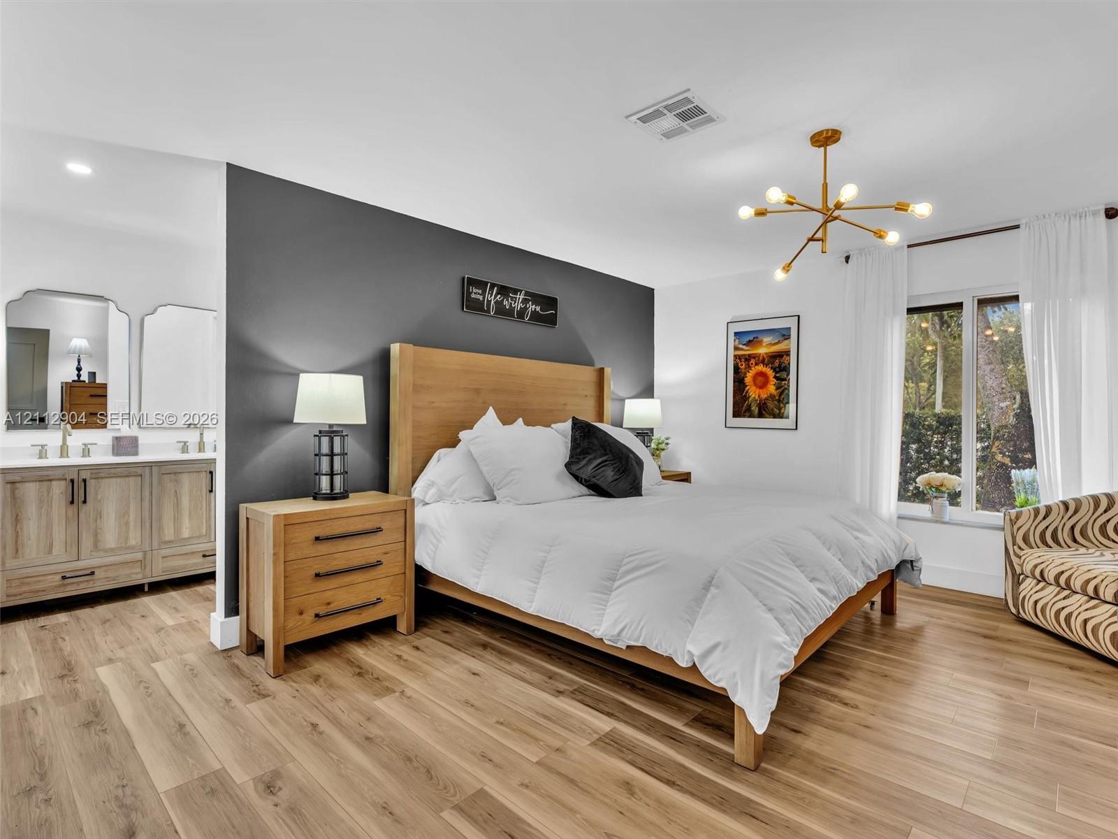 Wood-finish flooring, charcoal accent wall, multi-arm brass finish chandelier, and dual-sink vanity with framed mirrors