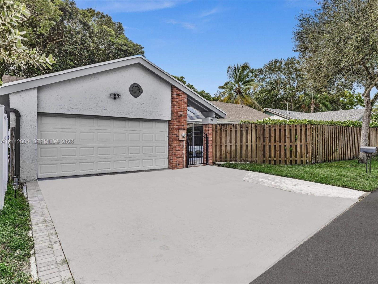 Single-story residence featuring a stucco facade, red brick accent siding, attached two-car garage, and wood-panel privacy fencing