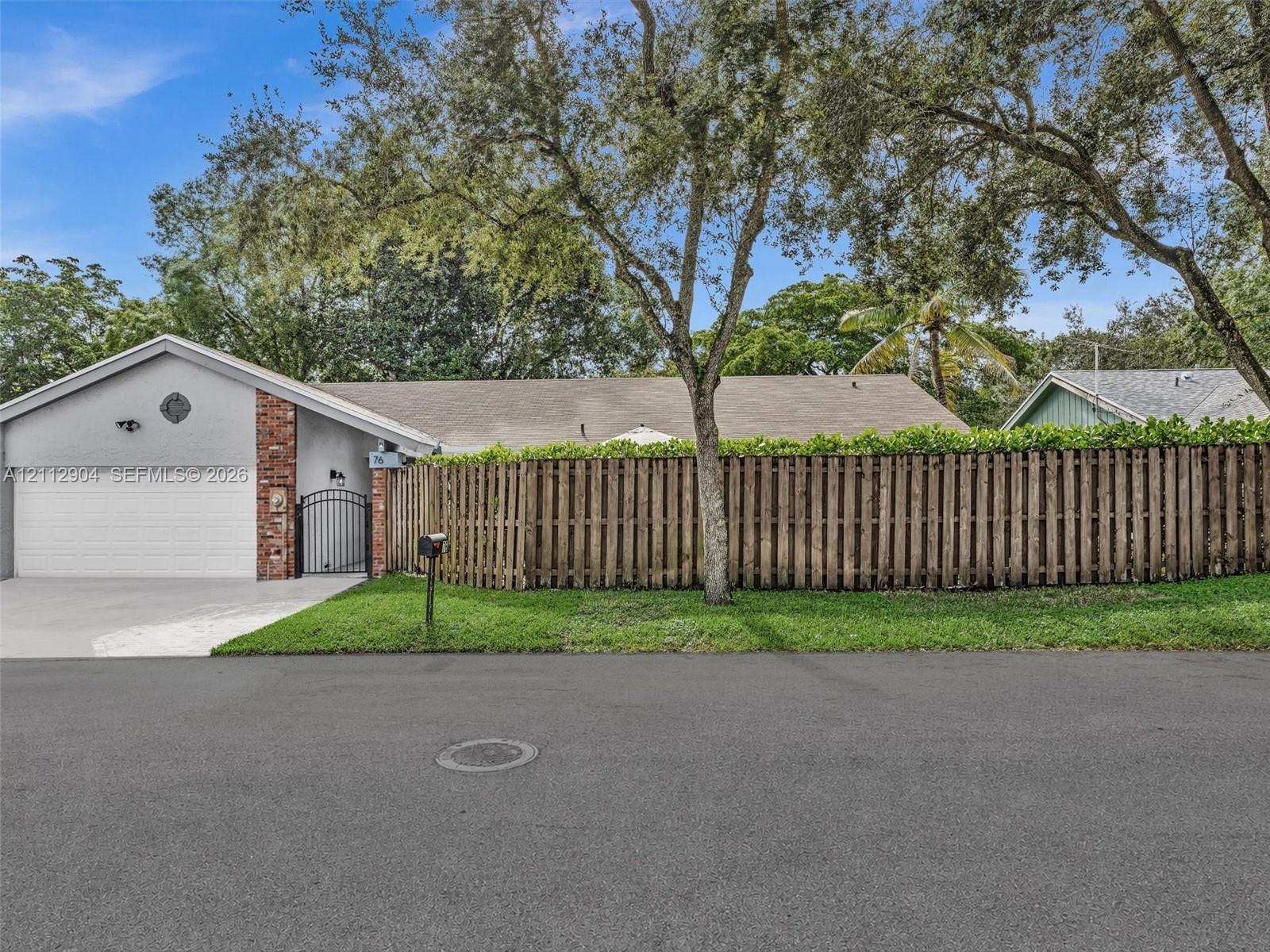 Single-story exterior featuring a stucco facade, red brick accents, an attached garage, and a wood privacy fence