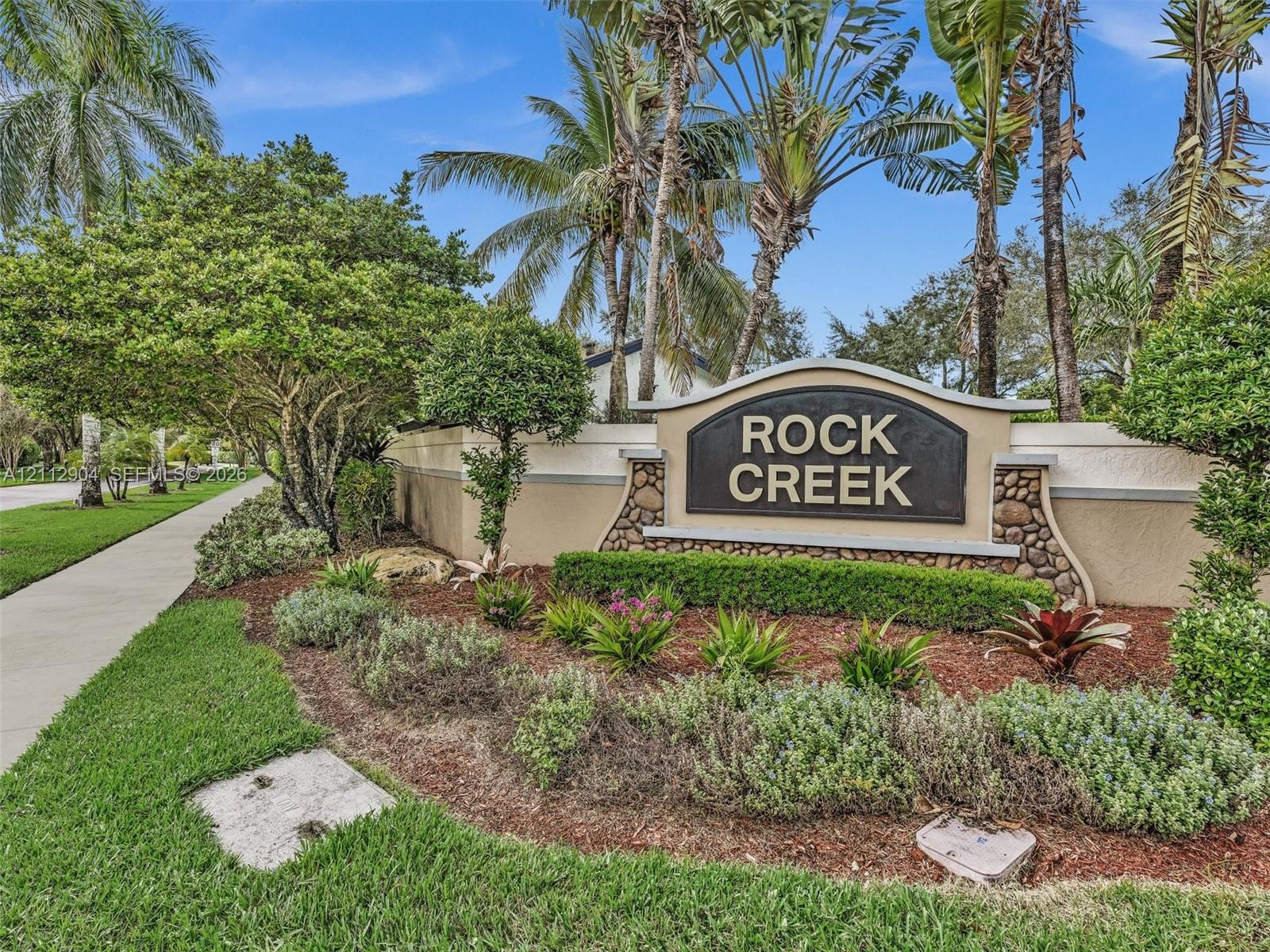 Community signage featuring stone masonry accents, professionally manicured landscaping, and mature palm trees