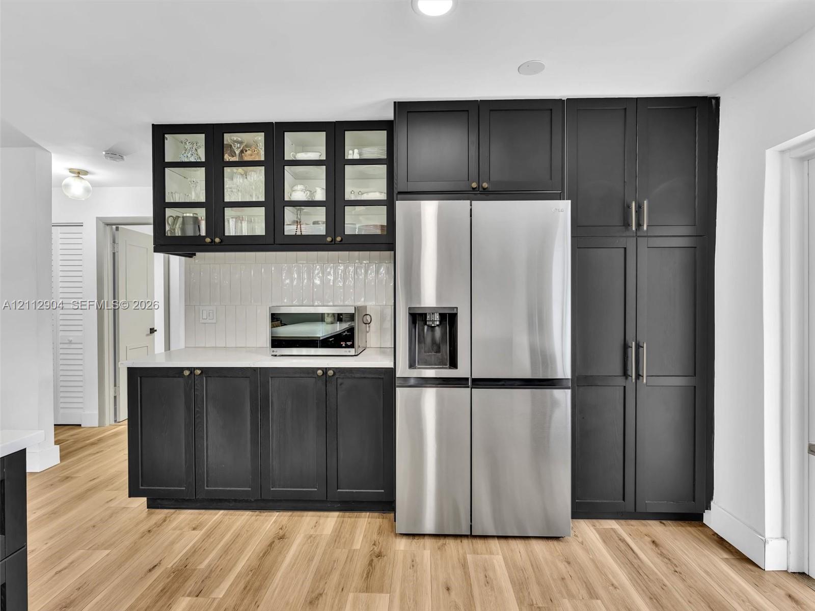 Custom cabinetry featuring glass-front upper storage, matte-finish lower cupboards, floor-to-ceiling pantry units, integrated stainless steel refrigeration, and wood-finish flooring