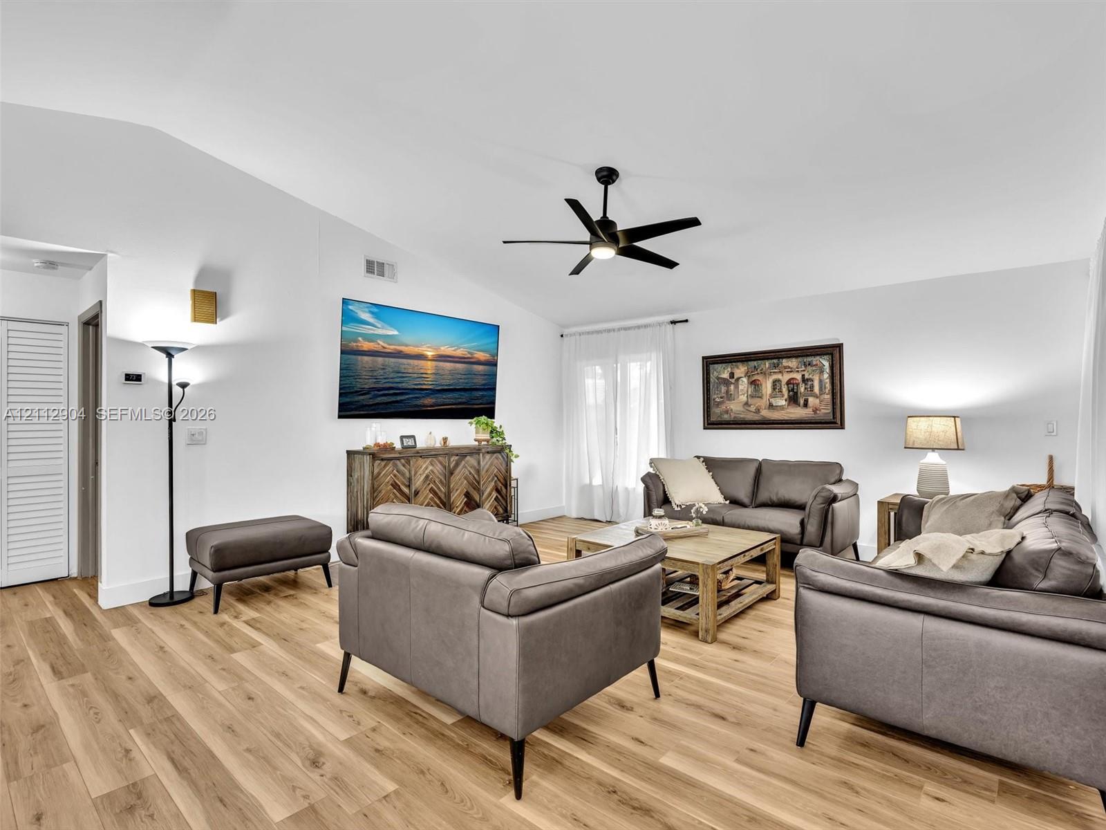 Living area featuring vaulted ceilings, wood-finish flooring, and a central ceiling fan with an integrated light fixture