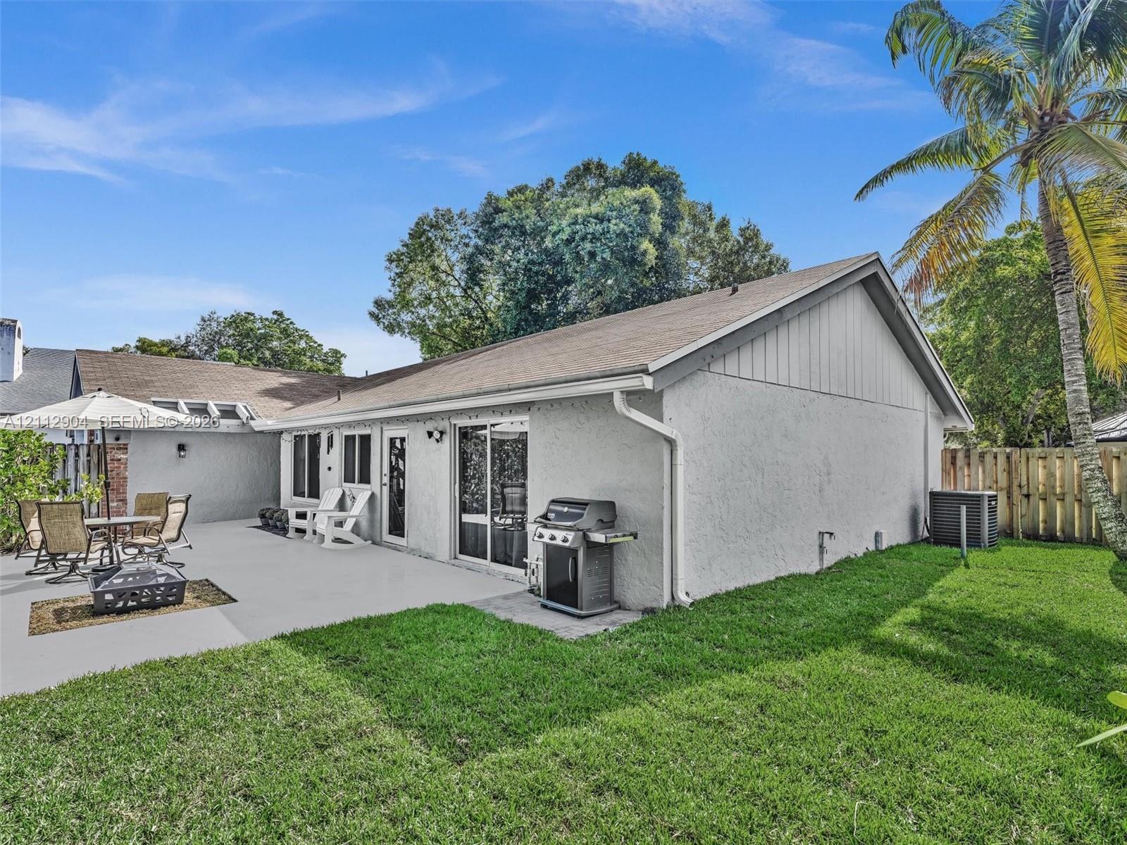 Stucco exterior with a rear concrete patio, sliding glass door, and fenced backyard featuring mature palm trees
