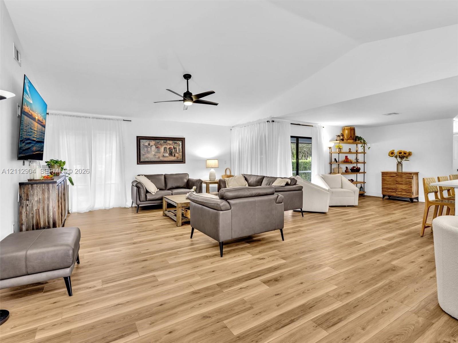 Vaulted ceilings, wood-finish flooring, and a contemporary ceiling fan in an open-concept interior with expansive sliding glass doors