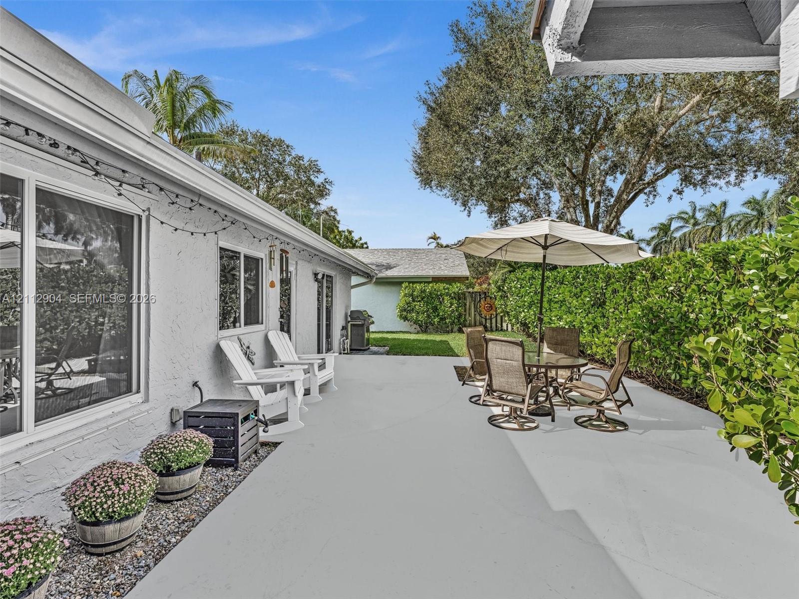 Concrete patio featuring painted finish, stucco exterior walls, sliding glass doors, and mature hedge perimeter