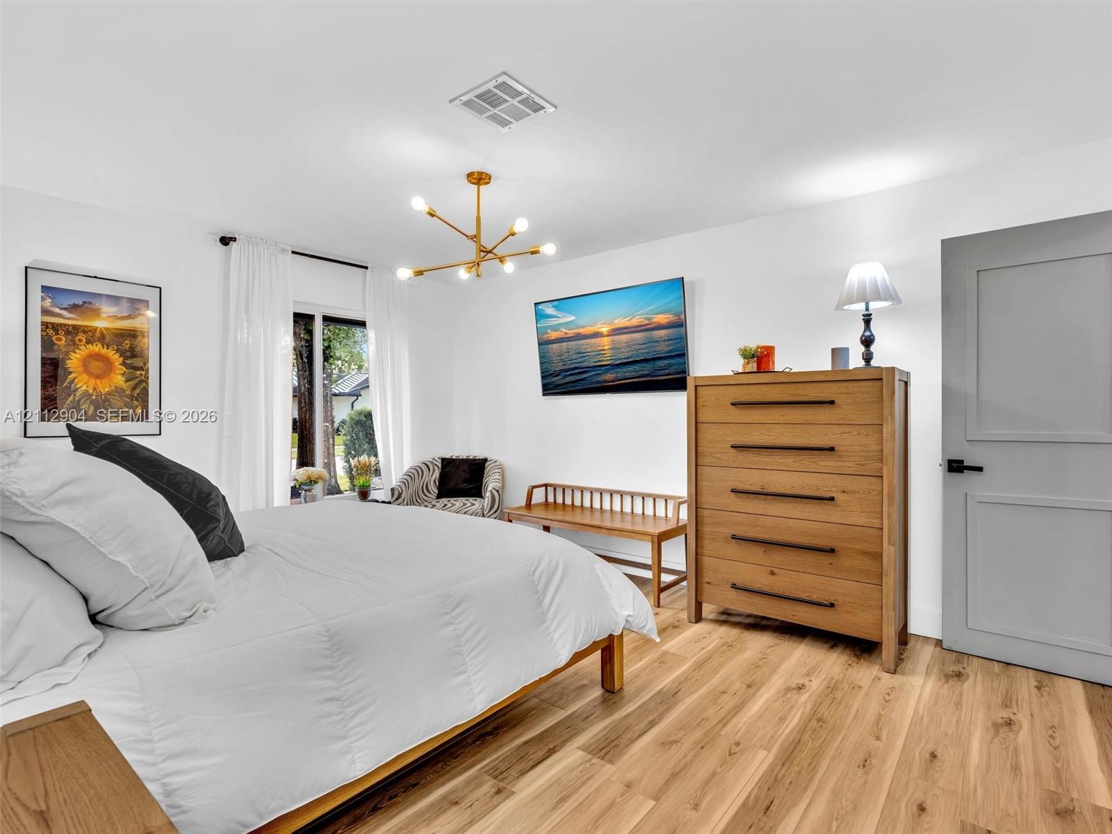 Wood-finish flooring, multi-arm brass chandelier, and grey-toned shaker-style interior door with matte black hardware
