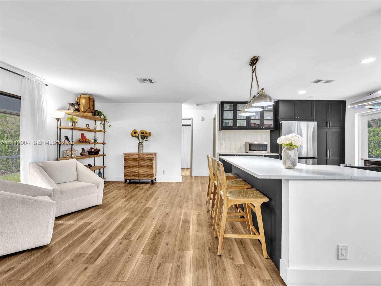 Open-concept kitchen featuring a large central island with quartz countertops, dark cabinetry, recessed lighting, and wood-finish flooring