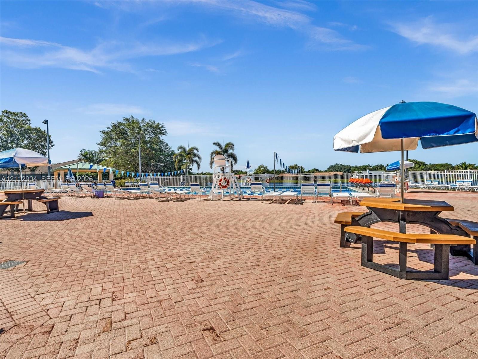 Swimming pool area with expansive paver deck, permanent picnic structures, and perimeter fencing