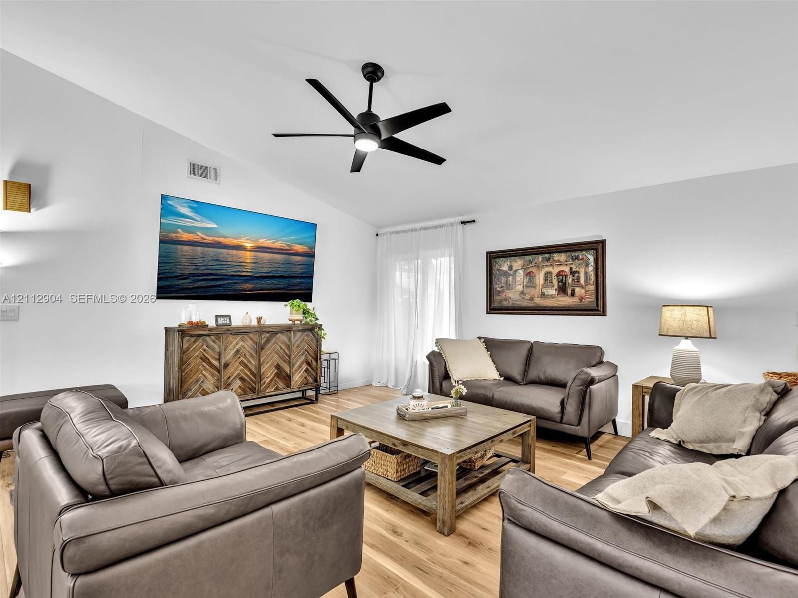 Vaulted ceilings, wood-finish flooring, and a contemporary matte black ceiling fan with integrated lighting
