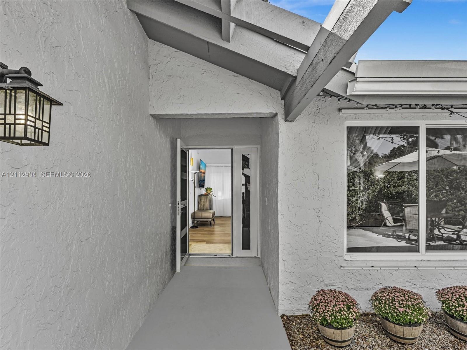 Covered entryway featuring textured stucco exterior, exposed rafters, decorative lantern-style wall lighting, and a glass-paneled front door