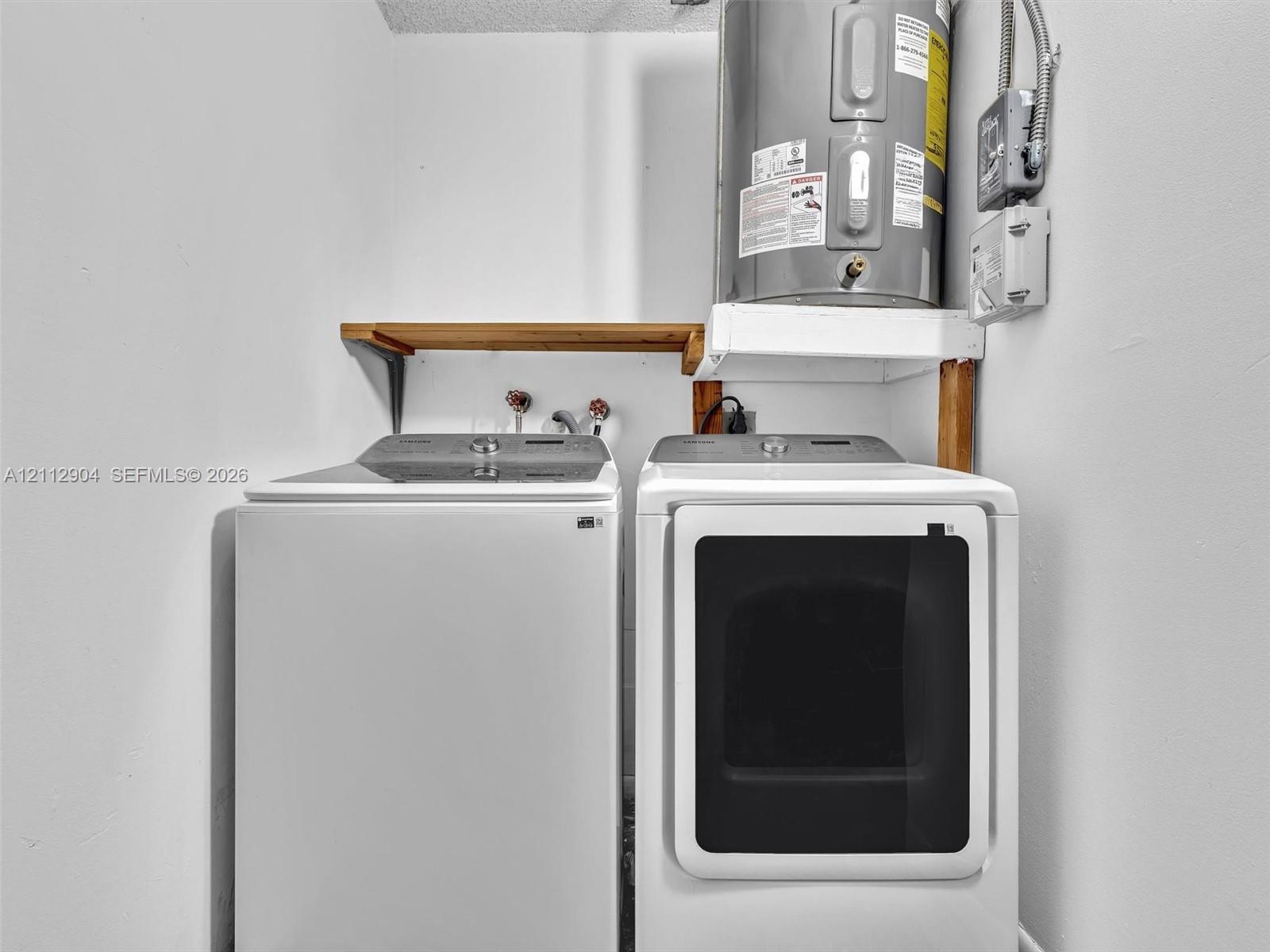 Utility area featuring an electric water heater, built-in wooden shelving, and dedicated hookups for laundry appliances