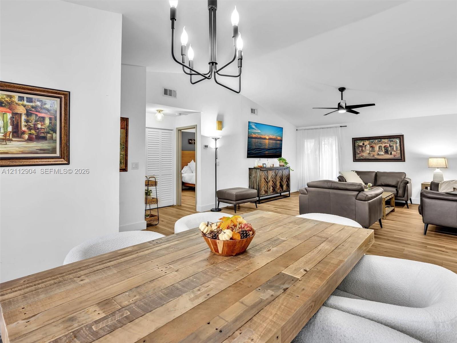 Open-concept living space featuring vaulted ceilings, wood-finish flooring, a multi-arm chandelier, and a black ceiling fan