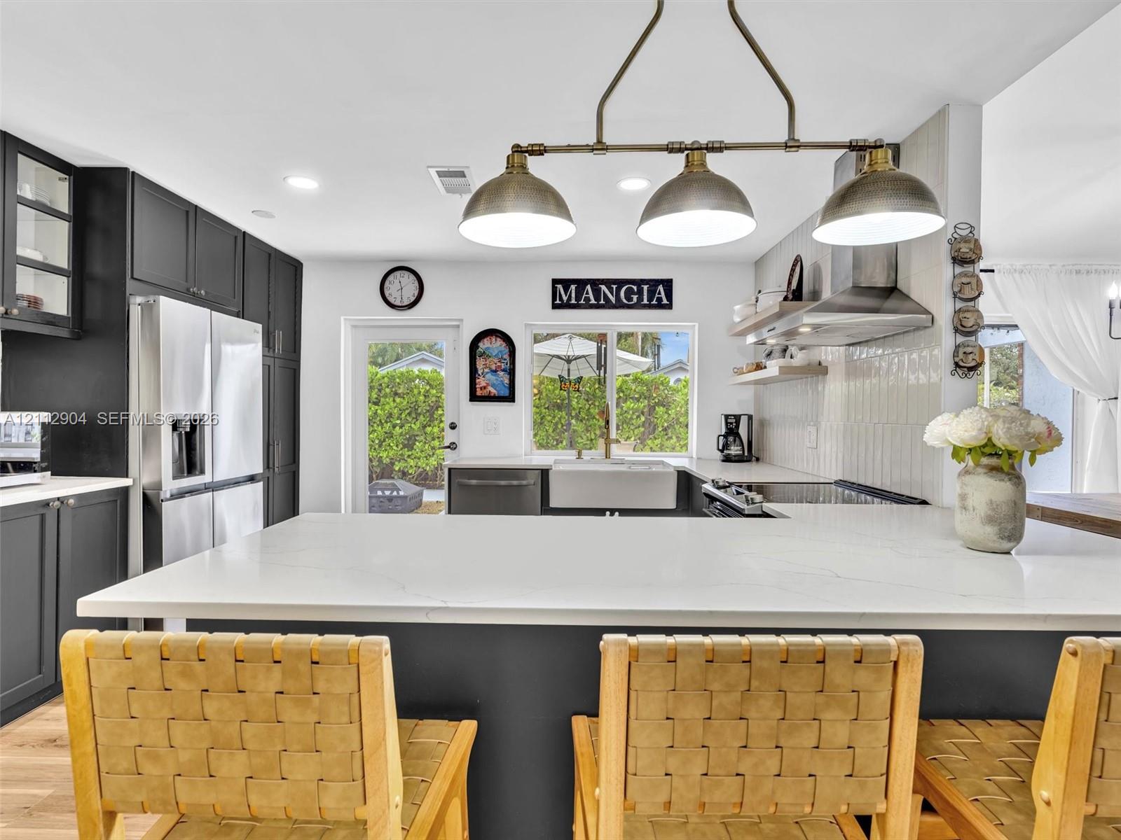 Kitchen featuring dark cabinetry, quartz countertops, a farmhouse-style sink, stainless steel range hood, and a multi-light pendant fixture