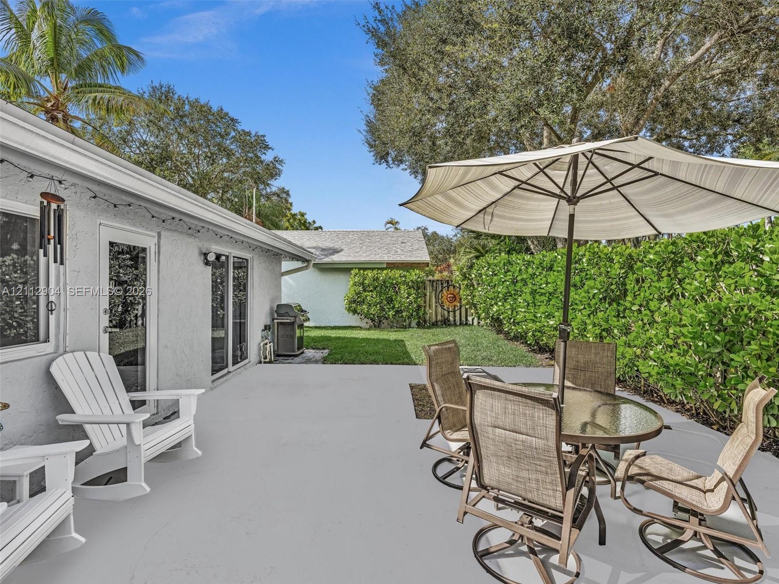 Concrete patio featuring sliding glass doors and manicured hedge perimeter