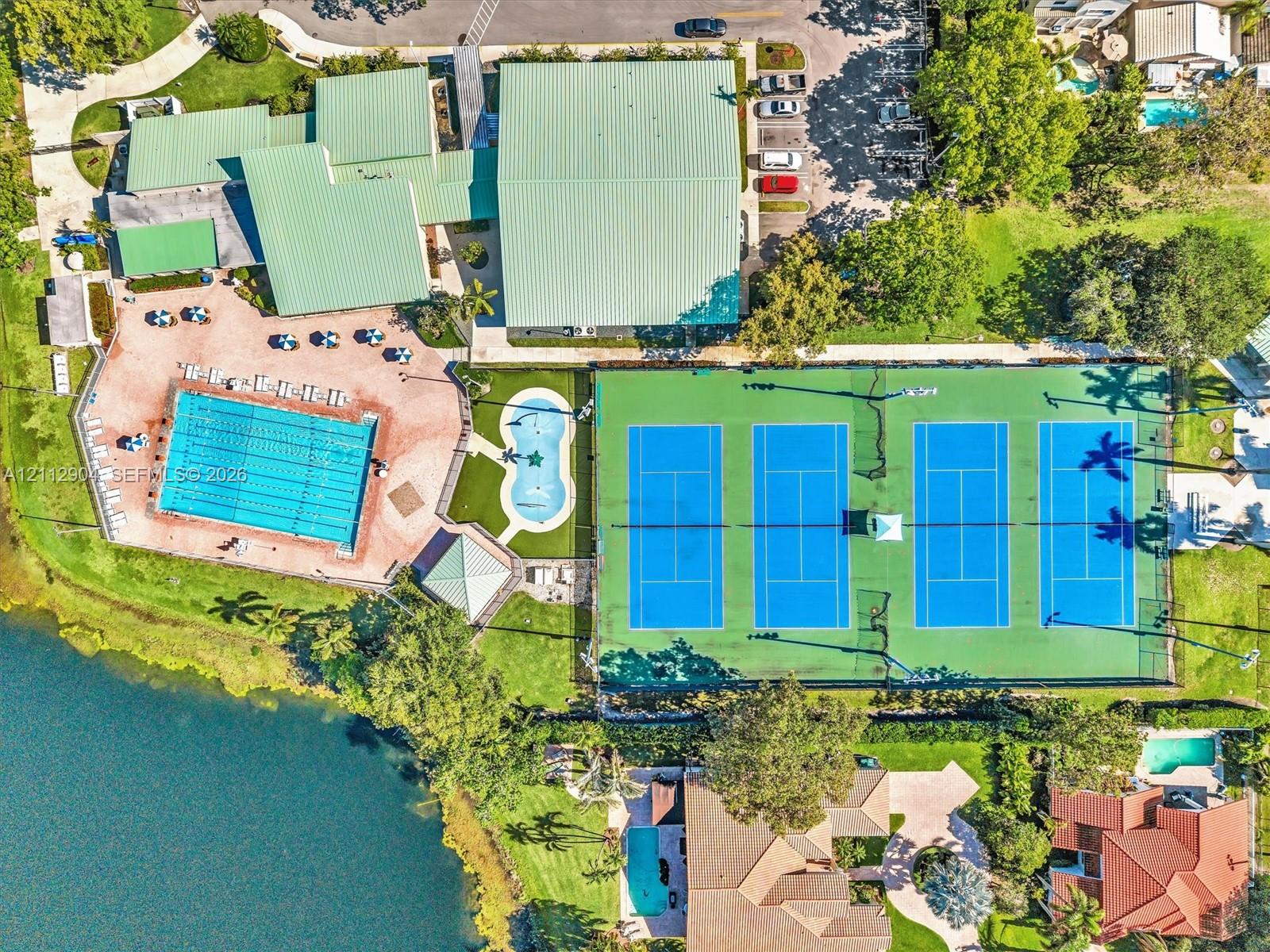Aerial perspective of recreational facilities featuring a swimming pool, separate small splash pool, four tennis courts, and waterfront access