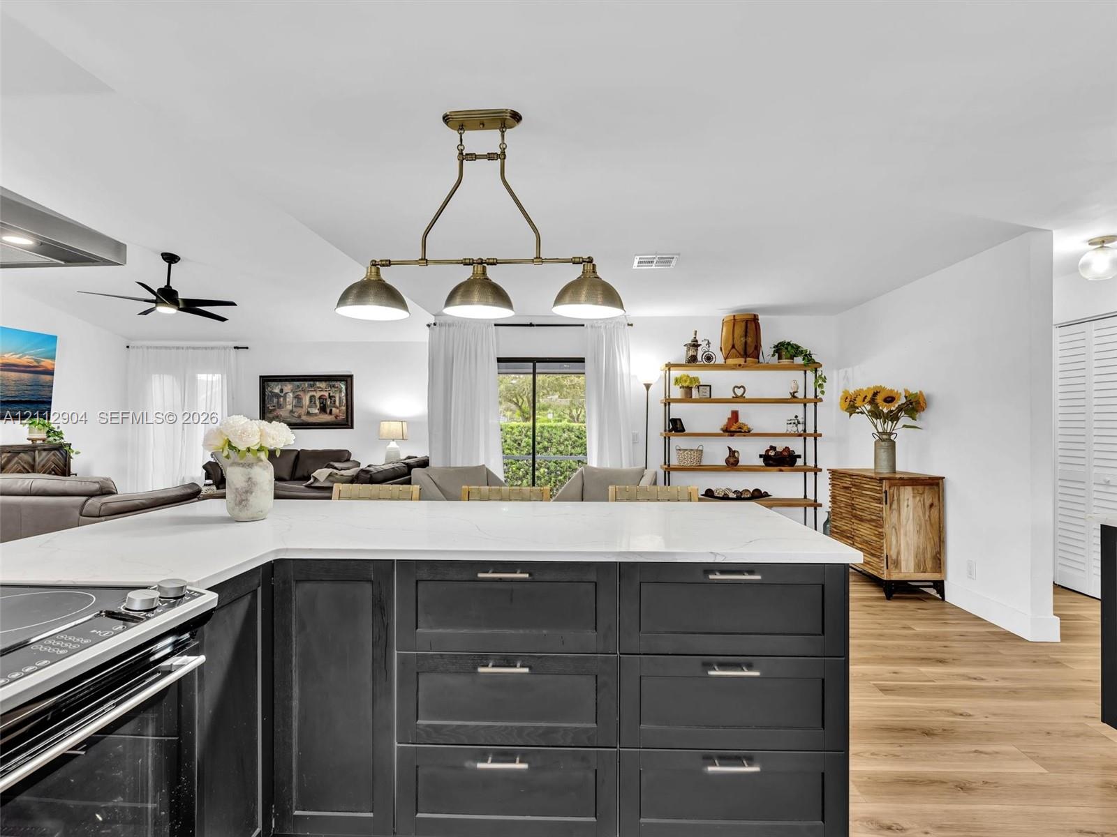 Kitchen featuring an L-shaped island with stone-finish countertops, matte black shaker-style cabinetry, wood-finish flooring, and a three-light metal pendant fixture