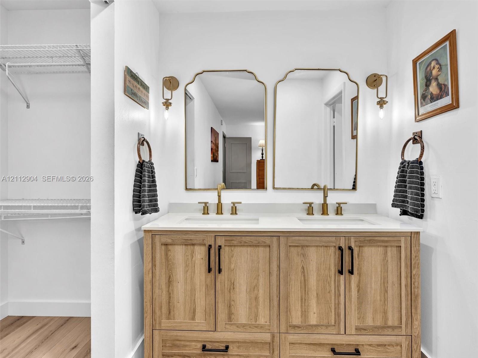 Double vanity featuring wood-finish cabinetry, solid surface countertop with integrated dual sinks, metallic finish faucets, and arched wall mirrors with wall-mounted light fixtures