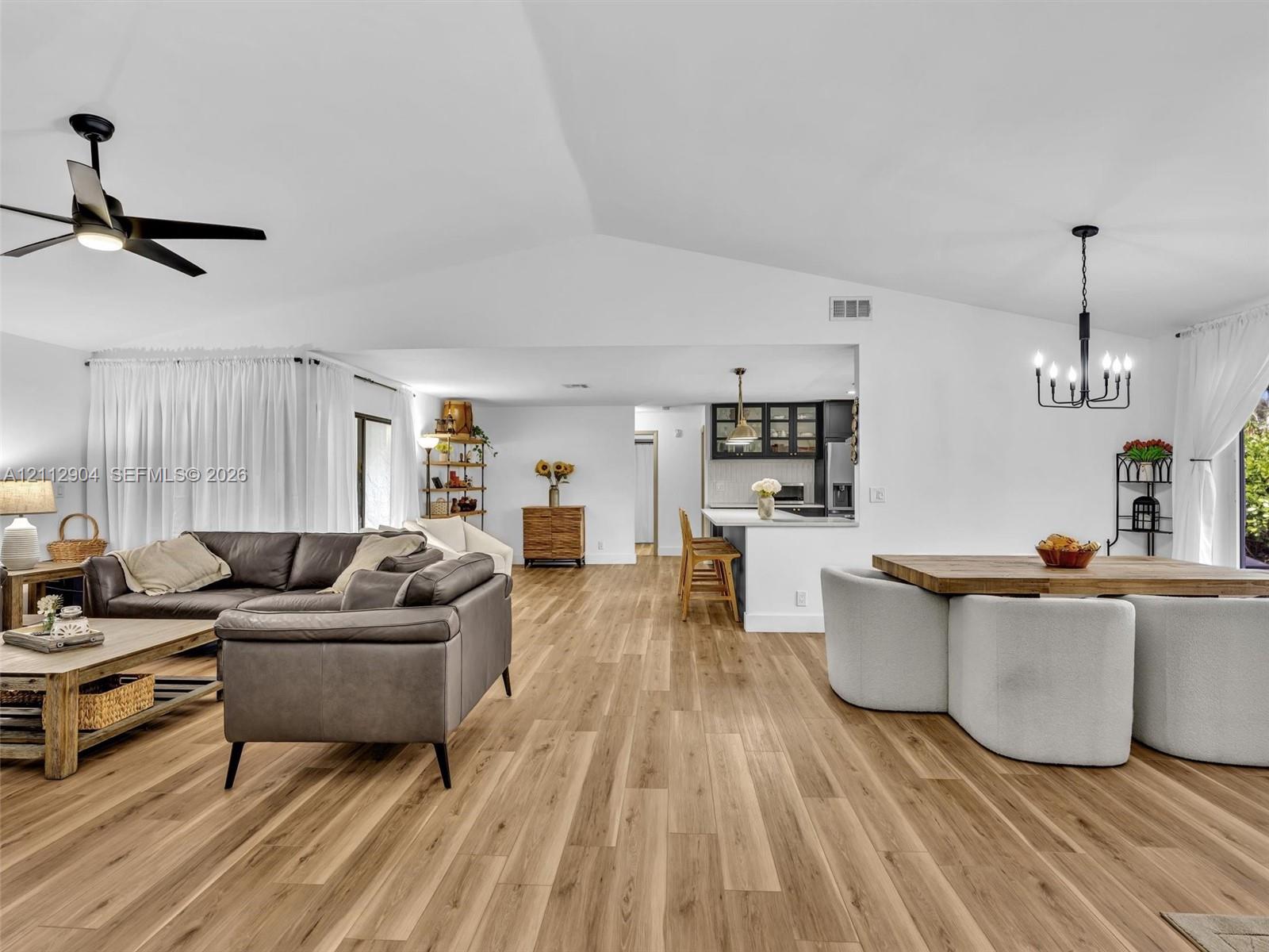 Vaulted ceilings, wood-finish flooring, recessed lighting, matte black ceiling fan, and a multi-arm chandelier