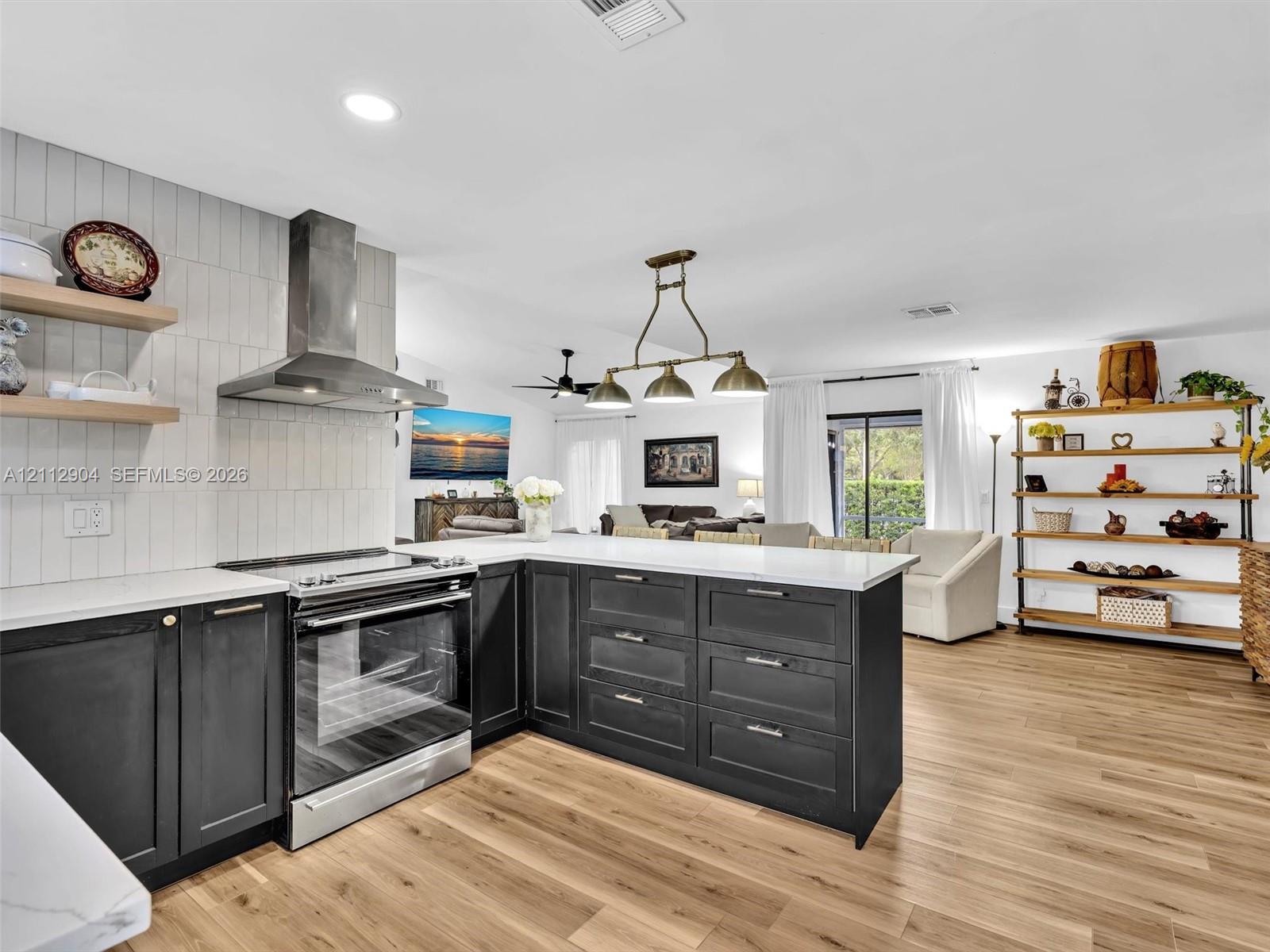 Kitchen featuring dark cabinetry, white countertops, vertical tile backsplash, stainless steel range with overhead hood, and wood-finish flooring